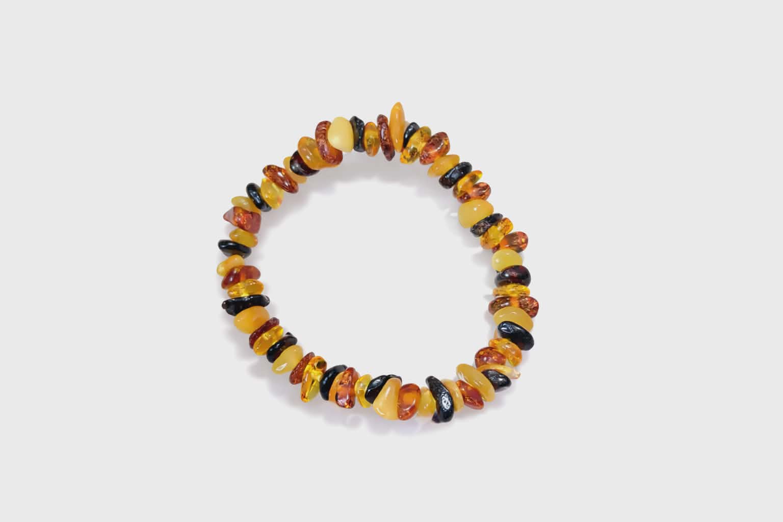Bracelet enfant en ambre naturel sur fond blanc, perles baroques miel, cognac et foncées, lumière douce, calme et énergie chaleureuse
