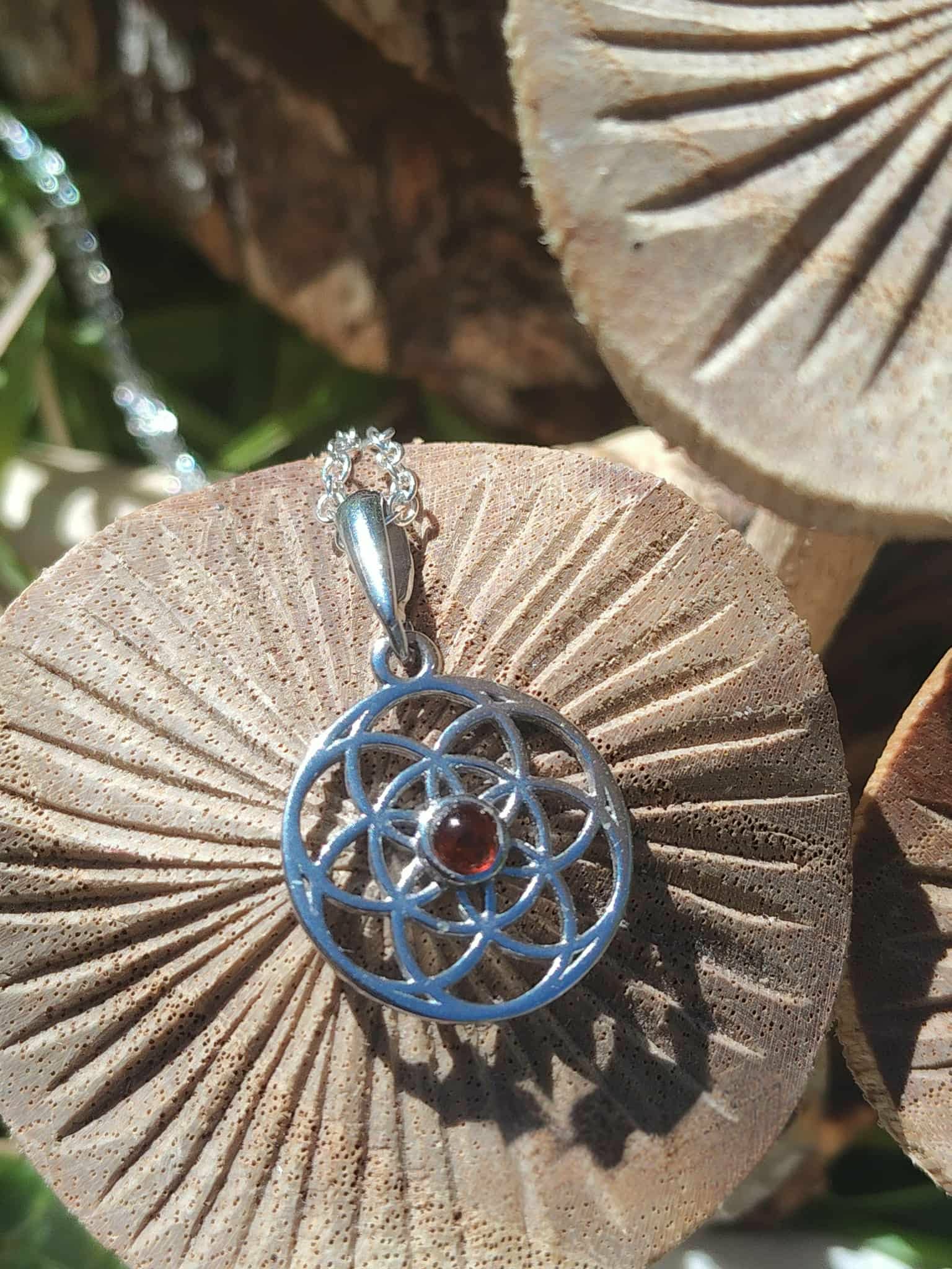 Pendentif Fleur de Vie en argent 925 avec perle d’ambre cognac posé sur décor champignons et bois en ambiance forêt, harmonie intérieure et chaleur lumineuse