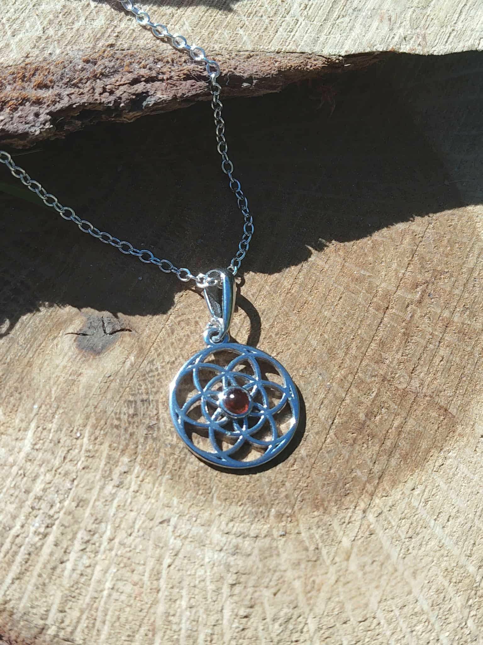 Pendentif Fleur de Vie en argent 925 avec perle d’ambre, suspendu sur une rondelle de bois au décor naturel ; symbole d’harmonie et d’équilibre, associé à la protection énergétique et à une sensation de clarté intérieure (bien-être).
