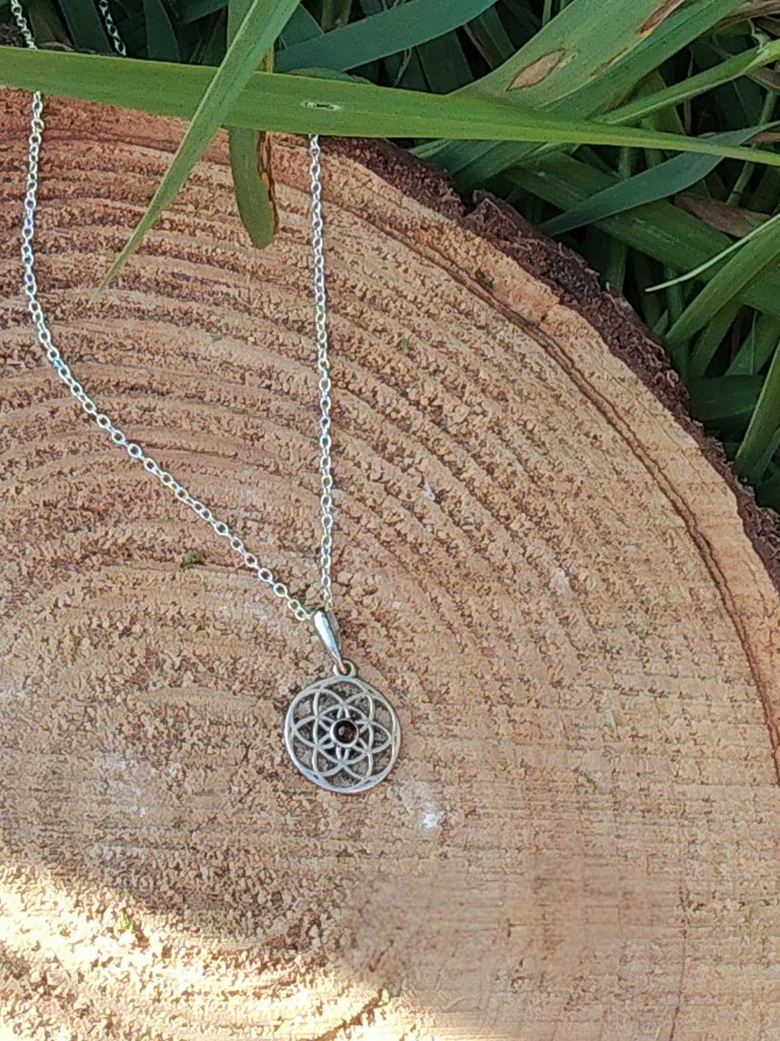 Pendentif Fleur de Vie argent 925 avec perle d’ambre suspendu sur rondin de bois et feuillage, harmonie naturelle et énergie positive