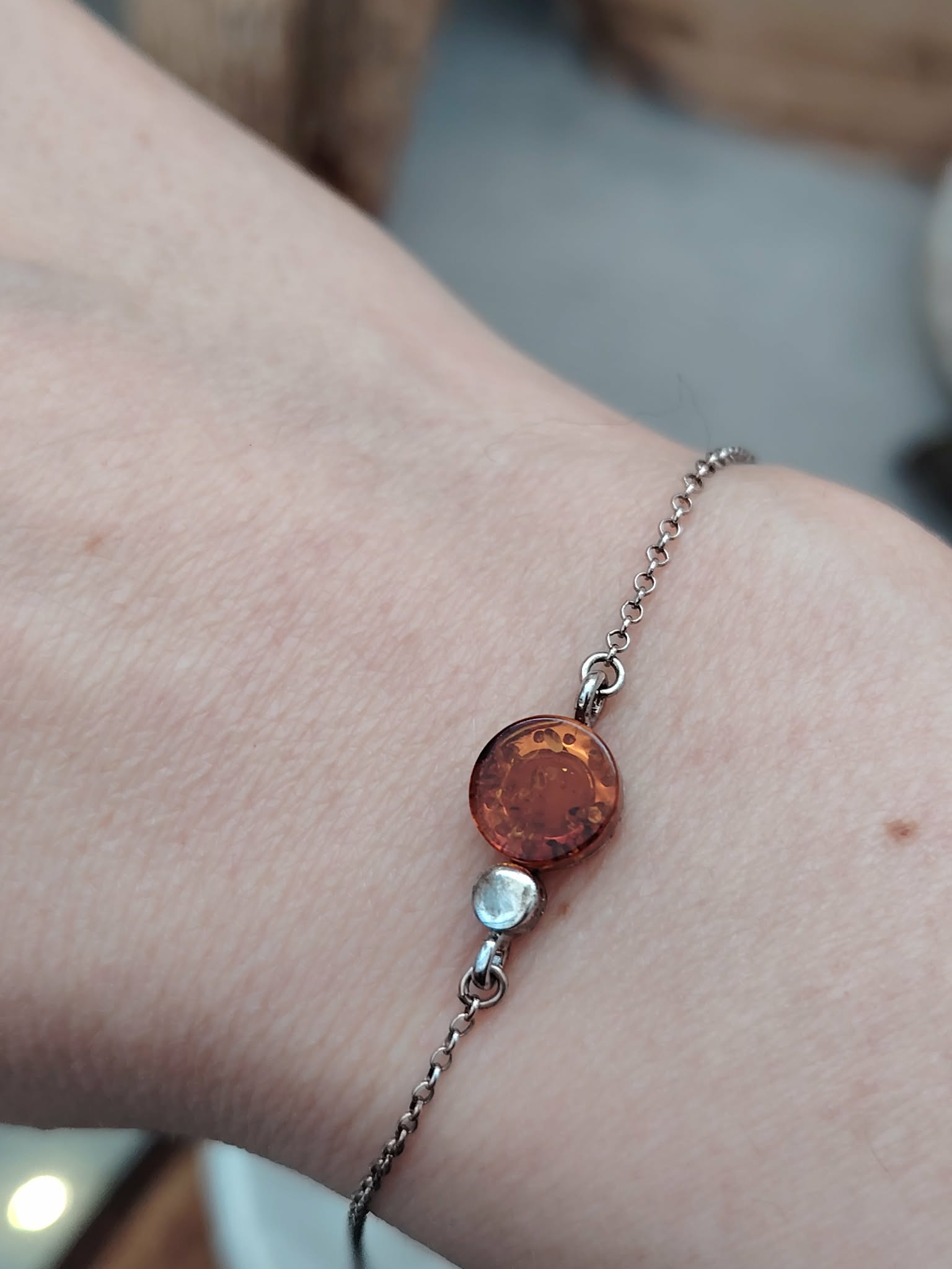 Bracelet ambre miel porté au poignet, chaîne fine en argent 925 rhodié avec cabochon rond, élégance lumineuse, détente émotionnelle et chaleur réconfortante.