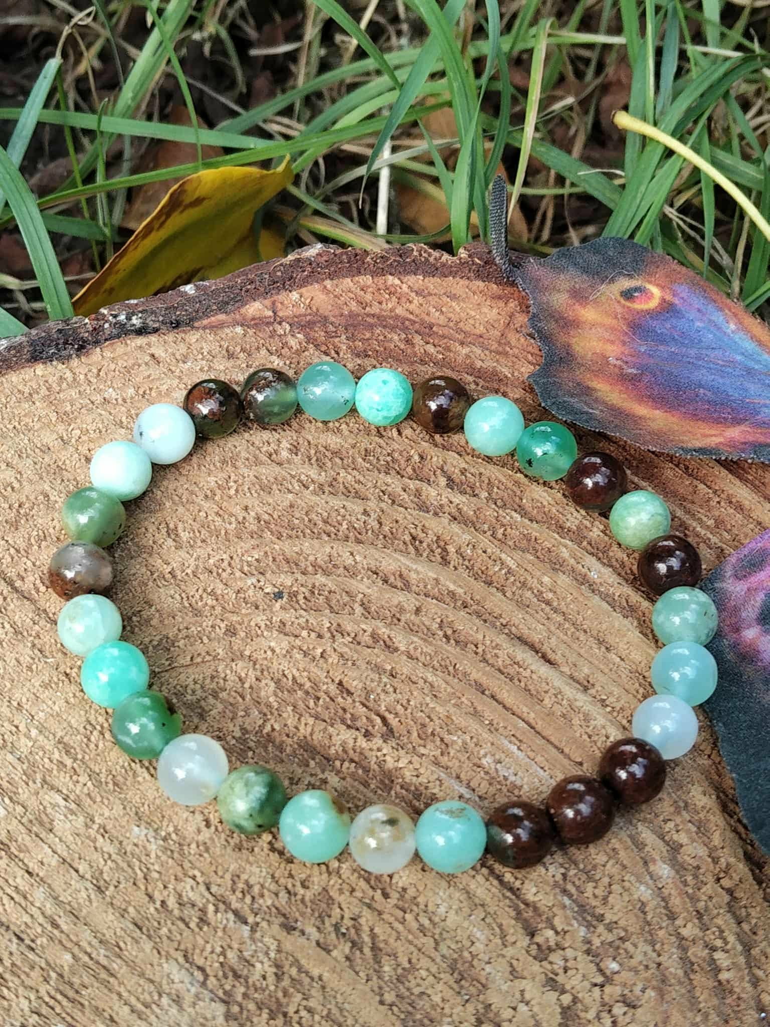Bracelet chrysoprase vert pomme et perles marron sur rondin de bois avec herbe et feuille brune, réconfort émotionnel et douceur du cœur