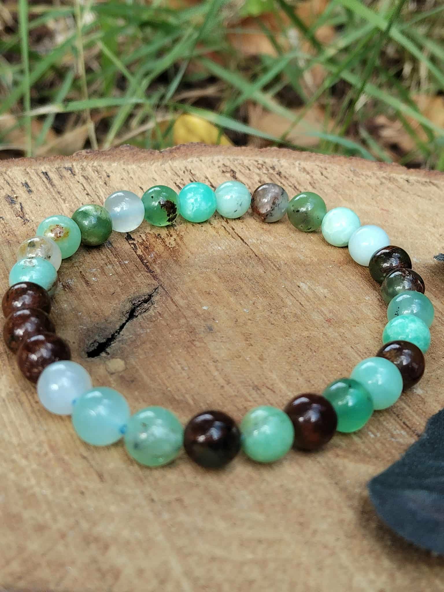 Bracelet chrysoprase sur tranche de bois avec verdure floue en arrière-plan, perles marron chocolat pour confiance calme et présence rassurée