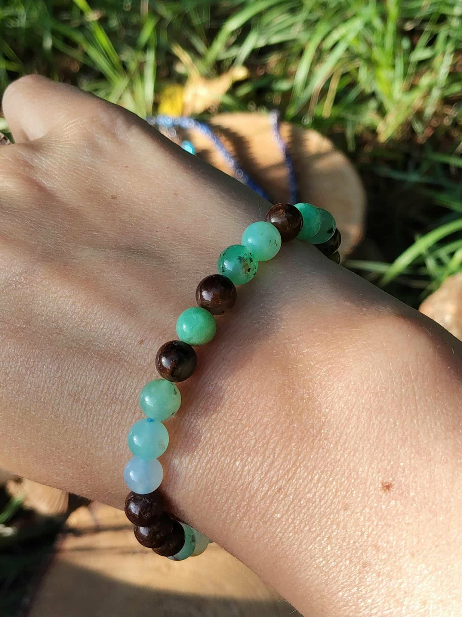 Bracelet chrysoprase porté au poignet, perles vertes et marron dans un décor d’herbes hautes et de feuilles, apaisement affectif et renouveau intérieur