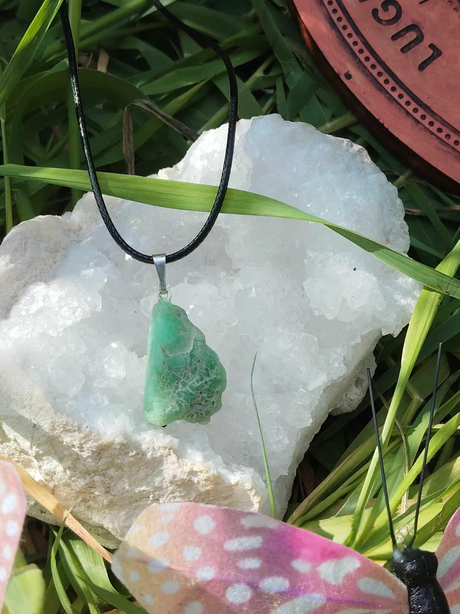 Pendentif chrysoprase verte sur cordon noir posé sur amas de quartz blanc avec feuilles vertes, pierre naturelle associée au calme intérieur, au renouveau et à la douceur du cœur.