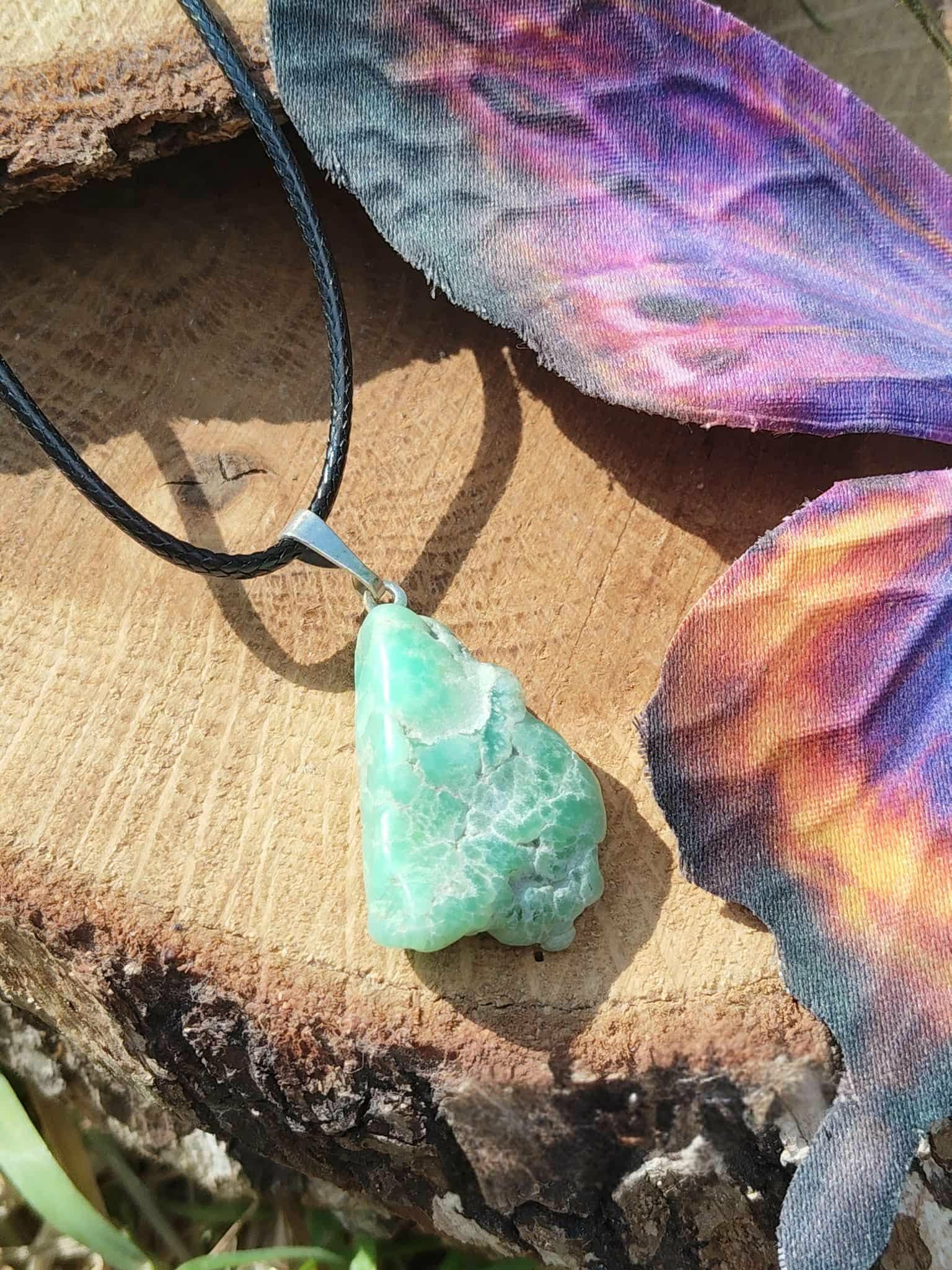 Pendentif chrysoprase pierre fine verte brute sur rondin de bois avec herbe au premier plan, bijou naturel évoquant la prise de recul, la lucidité douce et l’équilibre émotionnel.