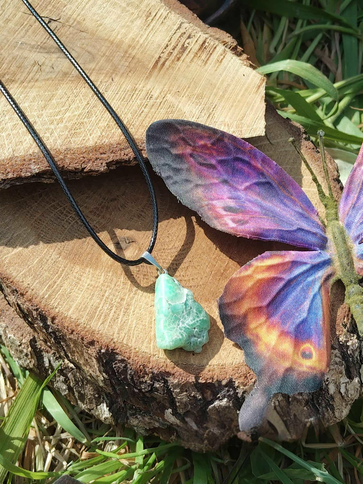 Pendentif chrysoprase naturelle vert d’eau sur cordon noir, décor rondins de bois et herbe, pierre fine verte évoquant la confiance tranquille, l’estime de soi et la fraîcheur émotionnelle.