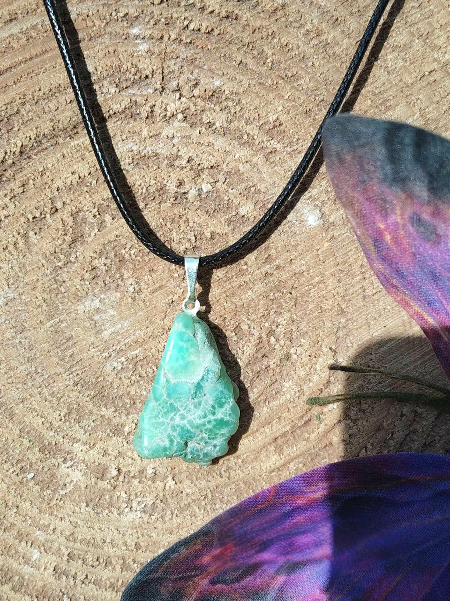 Pendentif chrysoprase pierre fine verte brute sur cordon noir, décor bois et papillon violet, bijou naturel évoquant l’assurance, l’ouverture affective et la légèreté intérieure.