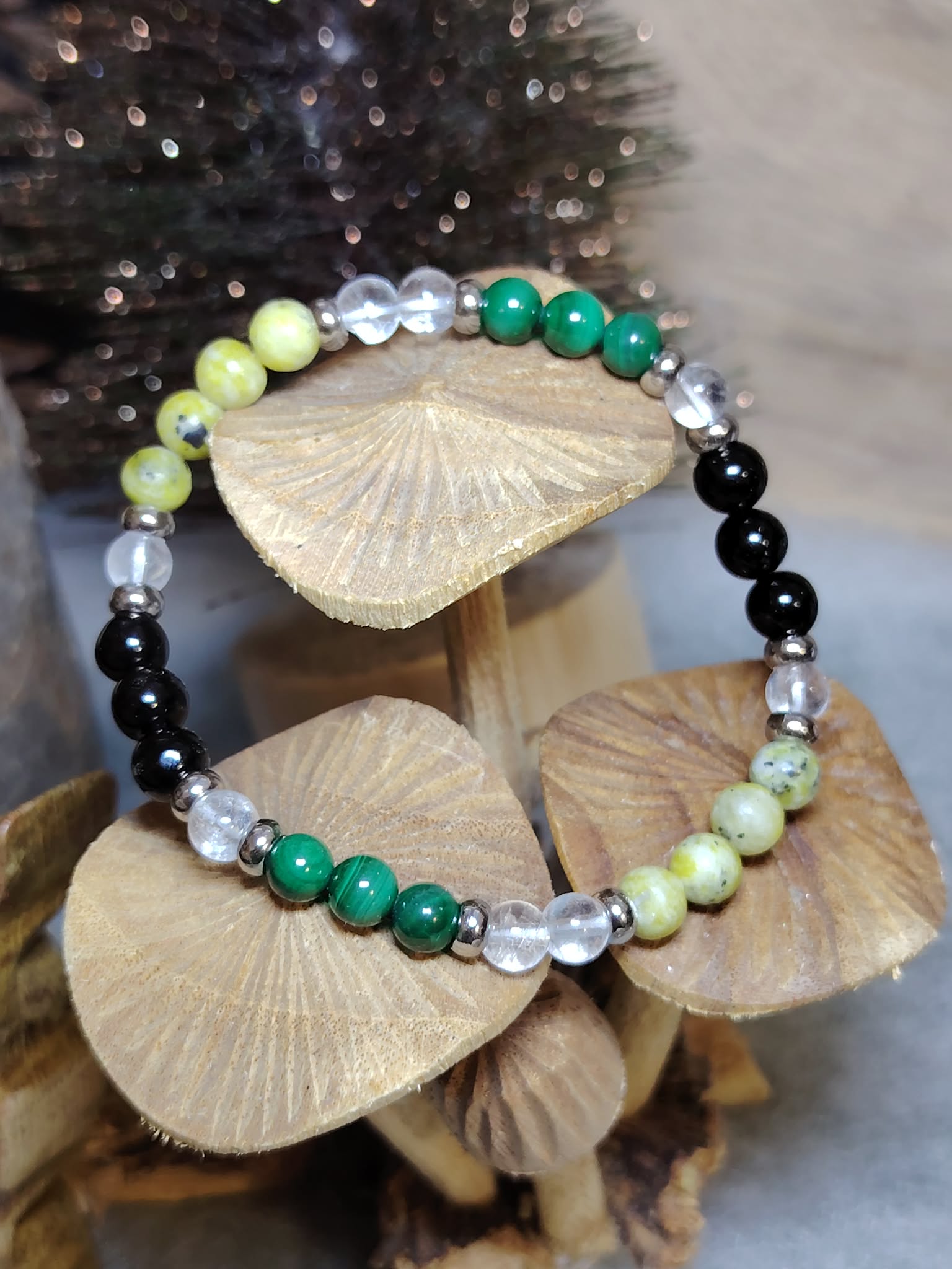 Bracelet Fibromyalgie malachite, serpentine et cristal de roche posé sur rondins, fond sombre, recentrage et stabilité émotionnelle
