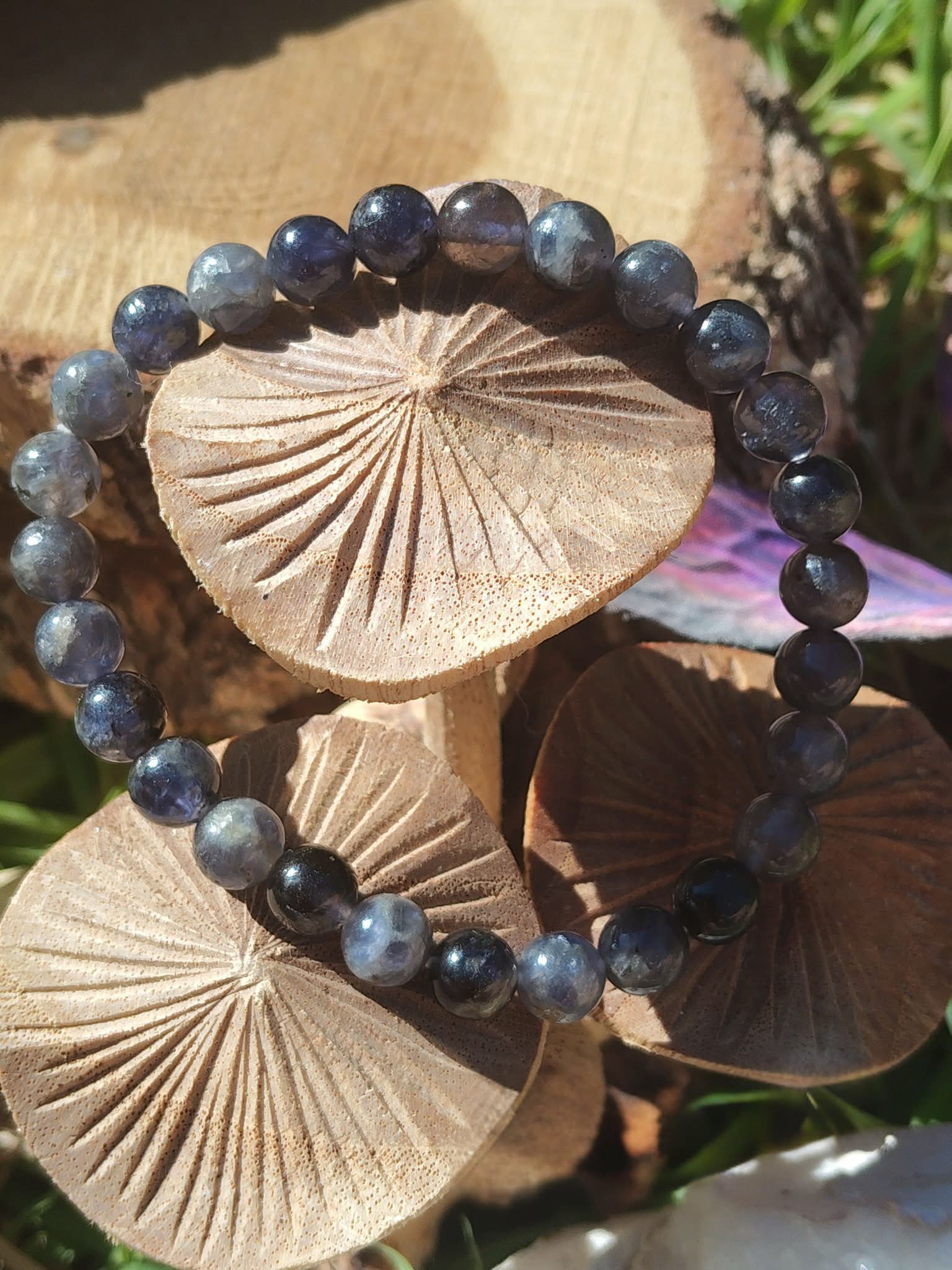 Bracelet iolite en gros plan sur décor forestier avec champignons en bois, nuances bleu-violet et gris ardoise pour stabilité mentale et respiration intérieure