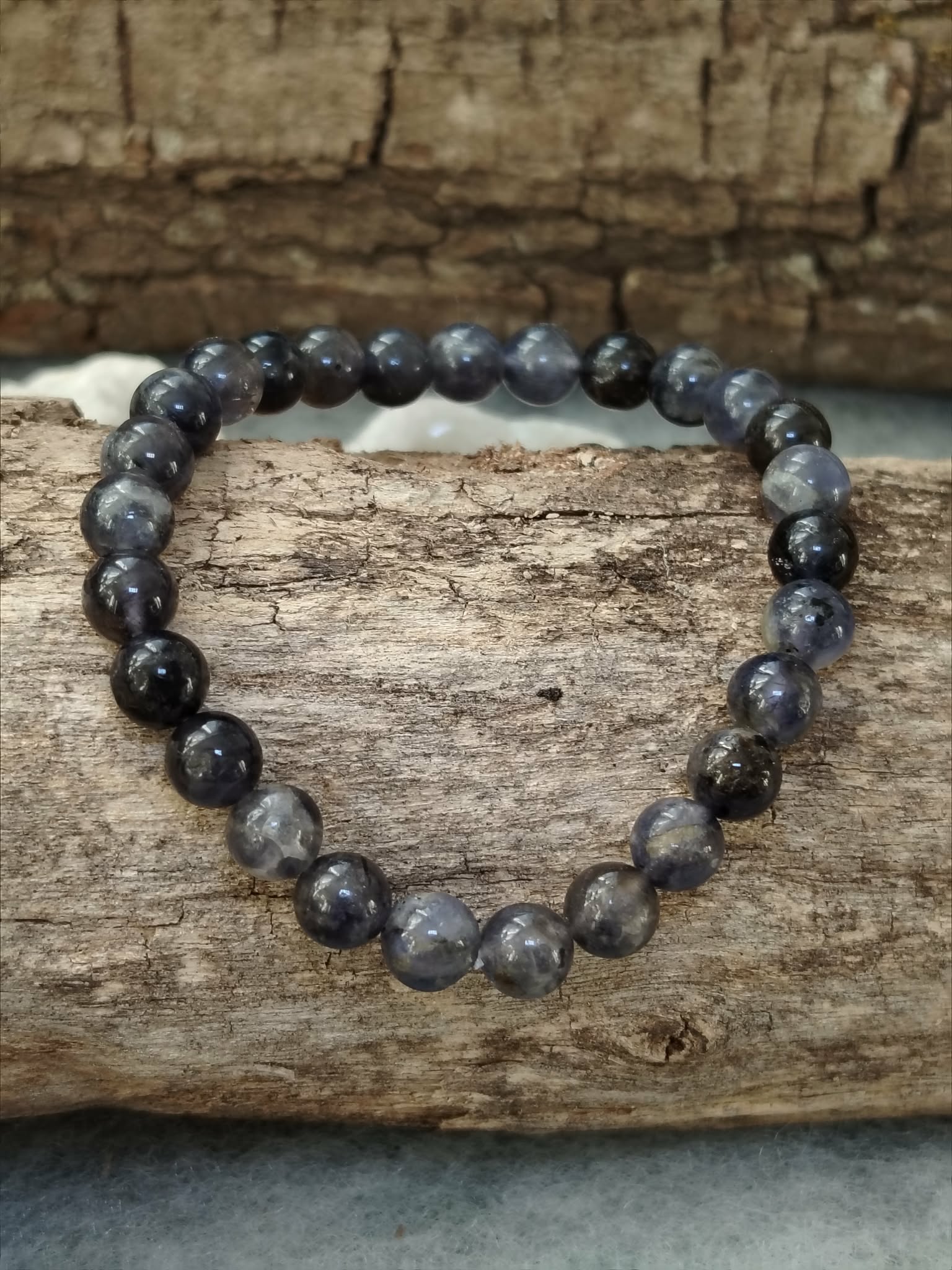 Bracelet iolite en pierre naturelle sur support en bois à l’ambiance rustique, perles bleu gris et indigo pour recentrage doux, relâchement et paix du mental