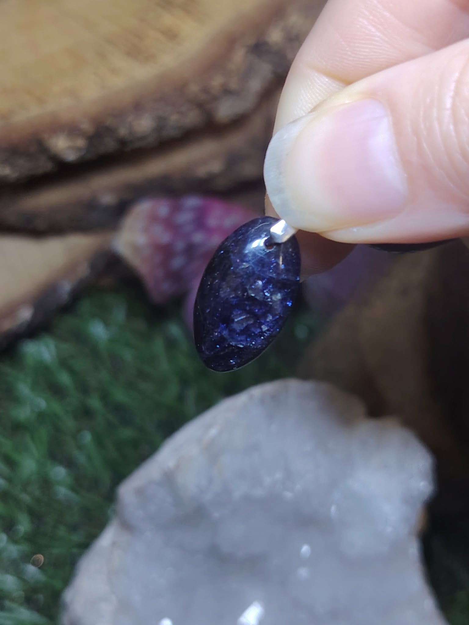 Pendentif iolite ou cordiérite en pierre naturelle, mis en scène avec minéraux clairs et verts, bijou associé à la clarté d’esprit, à l’apaisement et à l’équilibre intérieur.