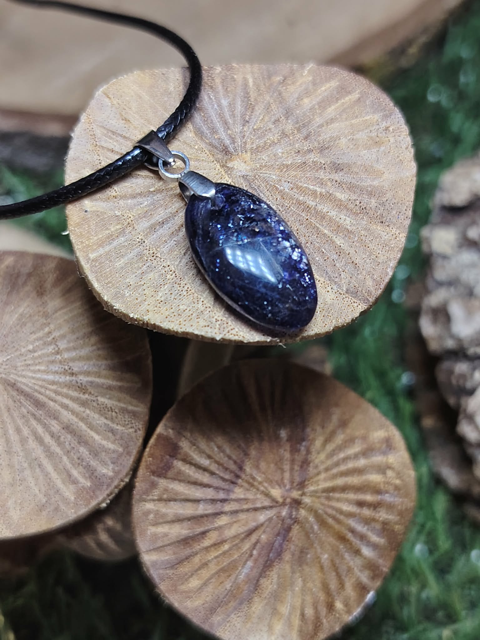 Pendentif iolite ou cordiérite sur cordon noir, posé sur champignons en bois striés, pierre naturelle aux nuances bleu-violet associée à l’écoute de soi, au recul et à la tranquillité intérieure.