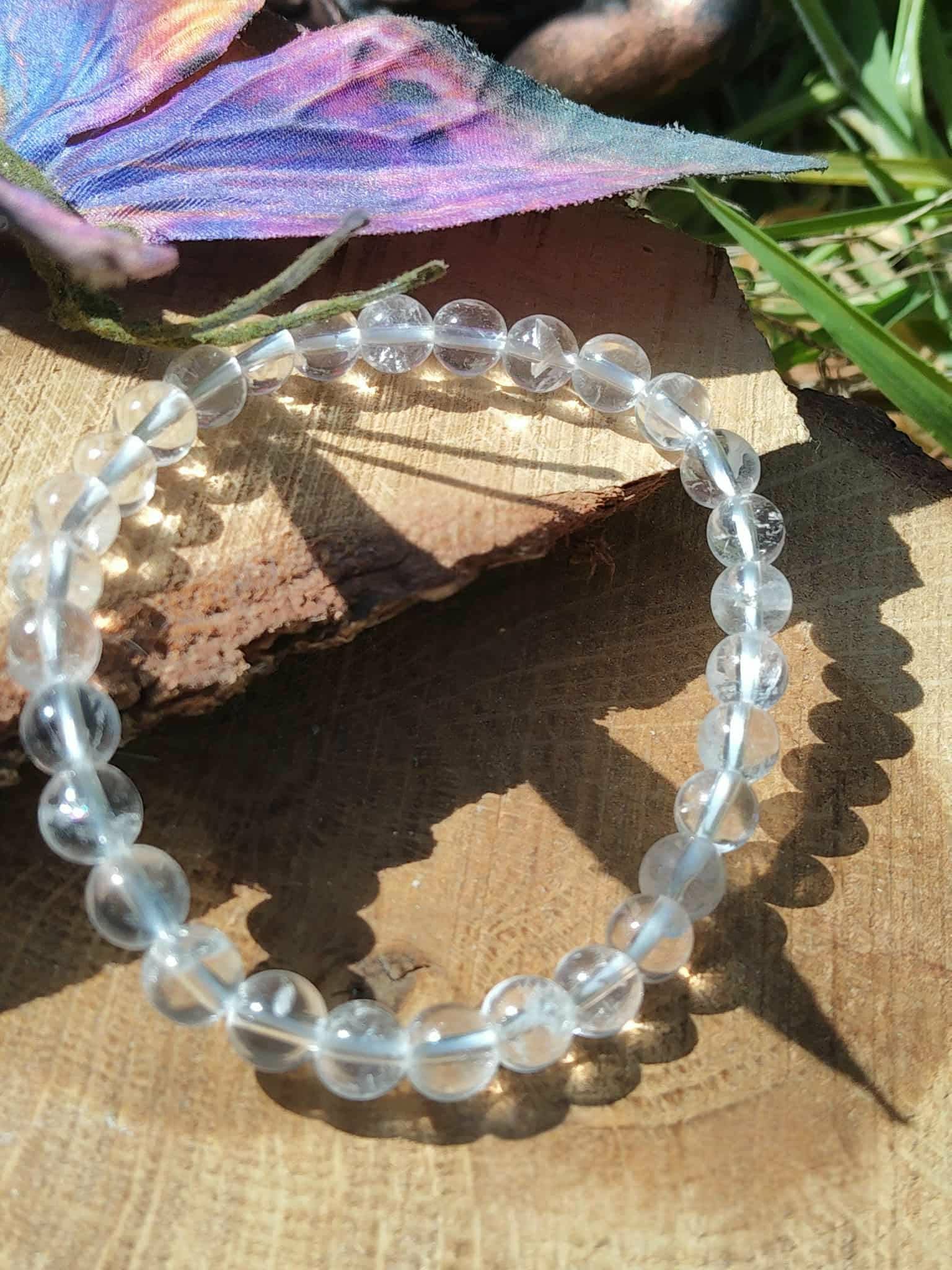 Bracelet pierre naturelle cristal de roche 6 mm posé sur bois en ambiance solaire, purification énergétique et sensation de fraîcheur intérieure