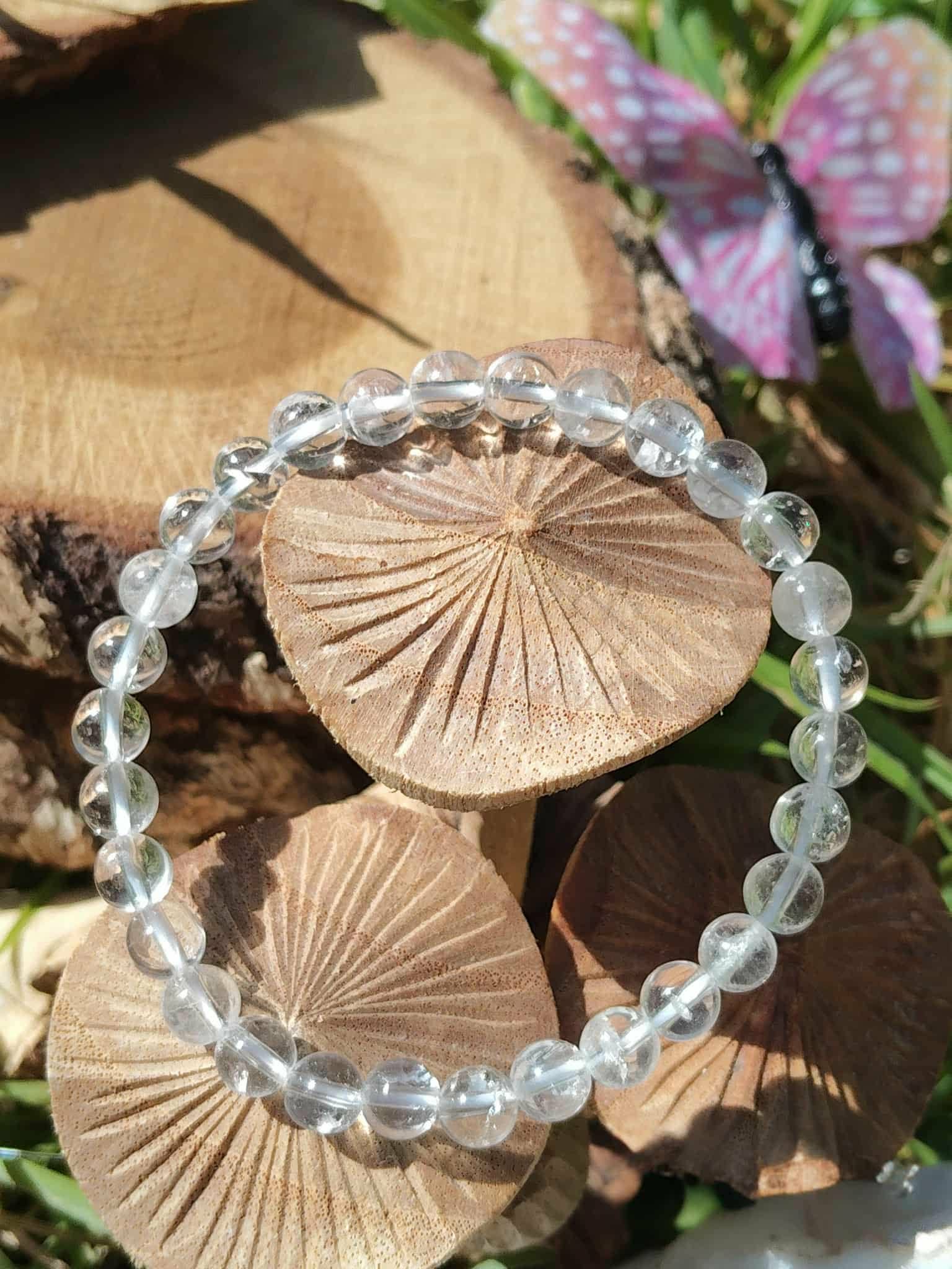Bracelet cristal de roche 6 mm en gros plan sur fond champignons en bois, perles translucides polies pour amplification des intentions et lucidité