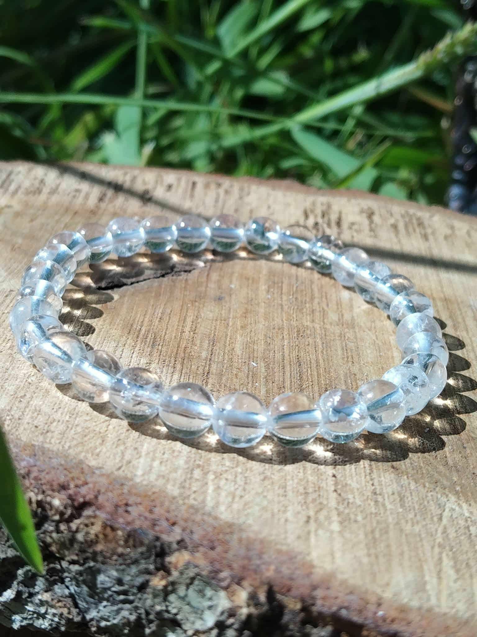 Bracelet cristal de roche 6 mm sur bois clair, transparence des perles mise en valeur dans une ambiance nature pour équilibre vibratoire