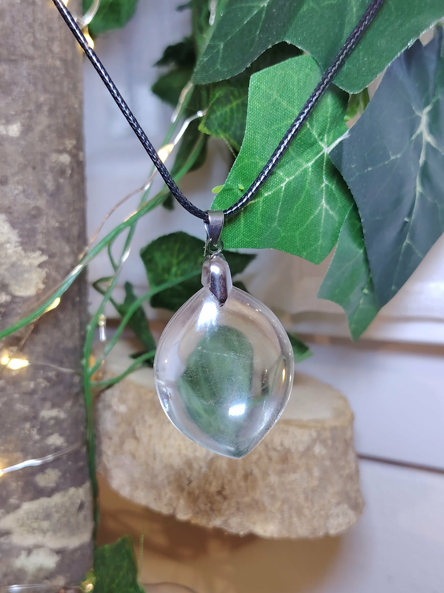 pendentif cristal de roche goutte en gros plan, transparence mise en valeur, décor lierre et sélénite — intuition