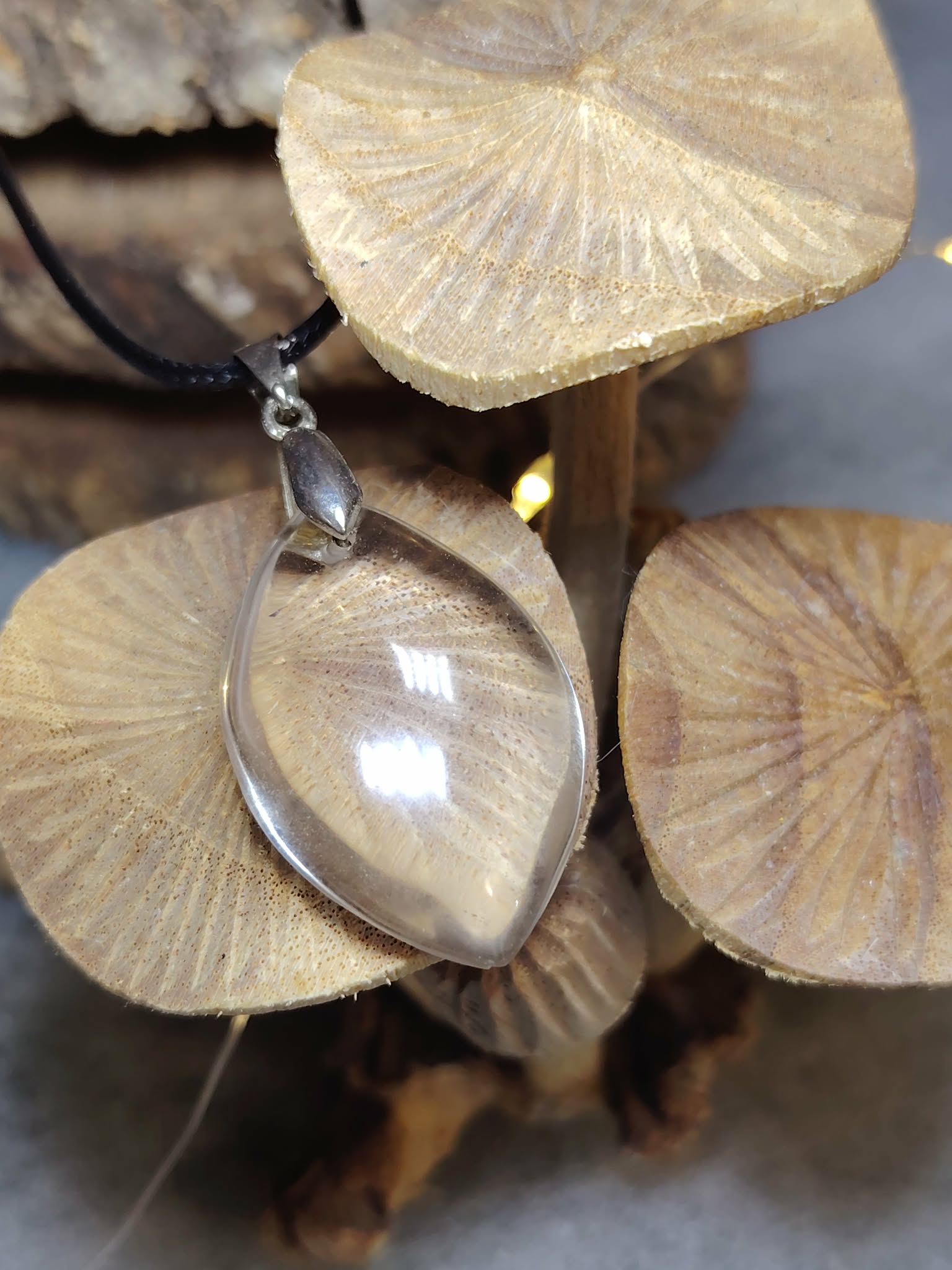 collier pendentif cristal de roche forme goutte sur bois brut avec rondins gravés, lumière douce, cordon noir visible — protection énergétique