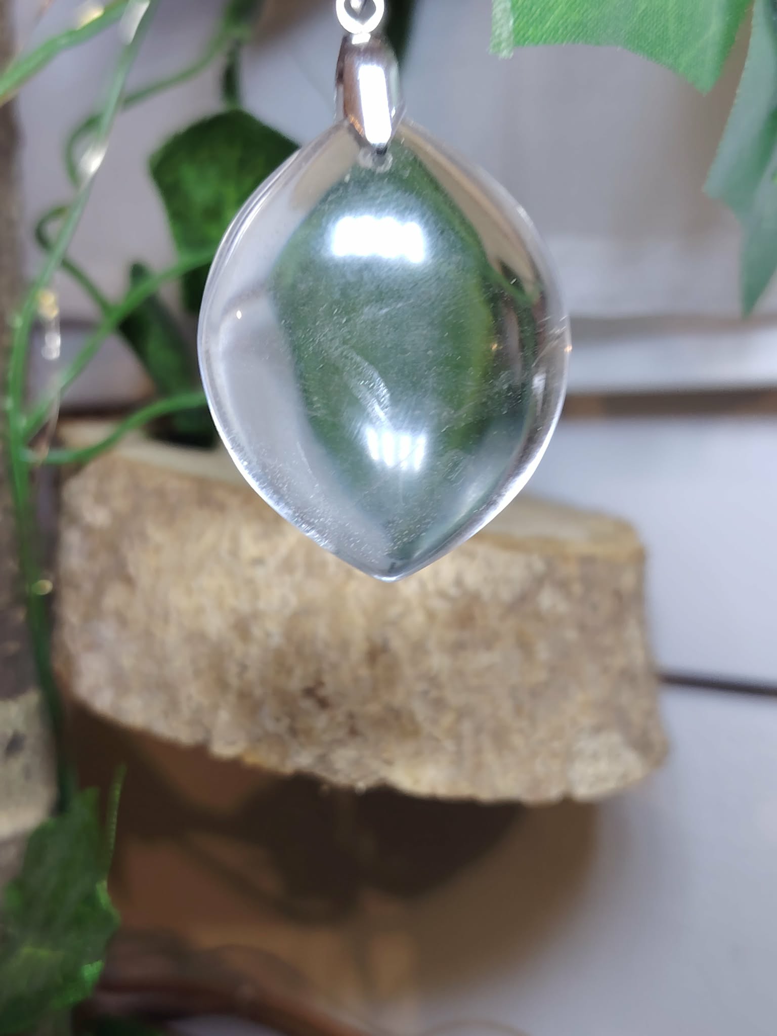 pendentif cristal de roche forme goutte en suspension, arrière-plan bois naturel et verdure, lumière douce — protection énergétique