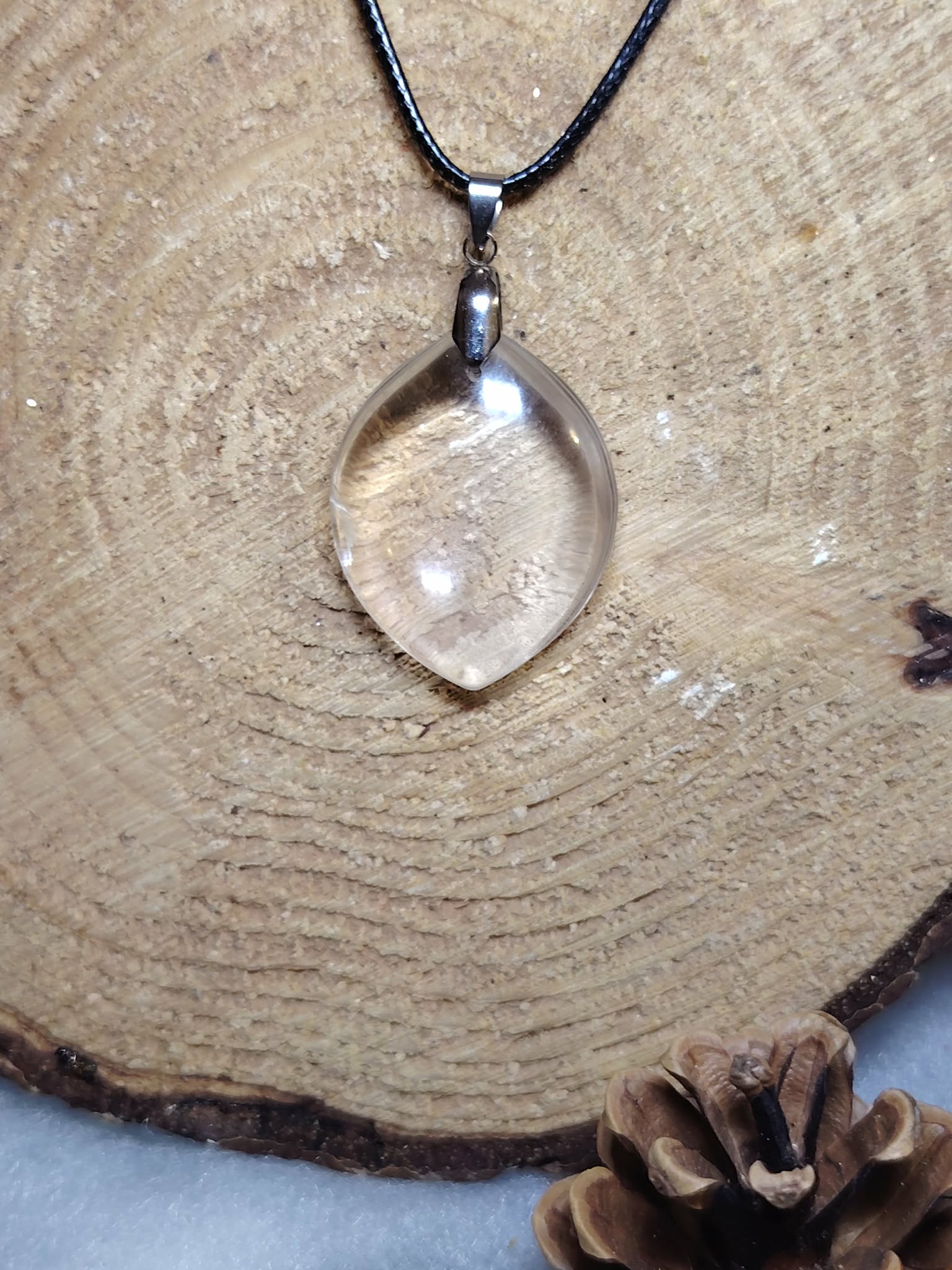pendentif quartz clair goutte centré sur support bois, pierre translucide lumineuse, cordon noir visible — amplification des énergies