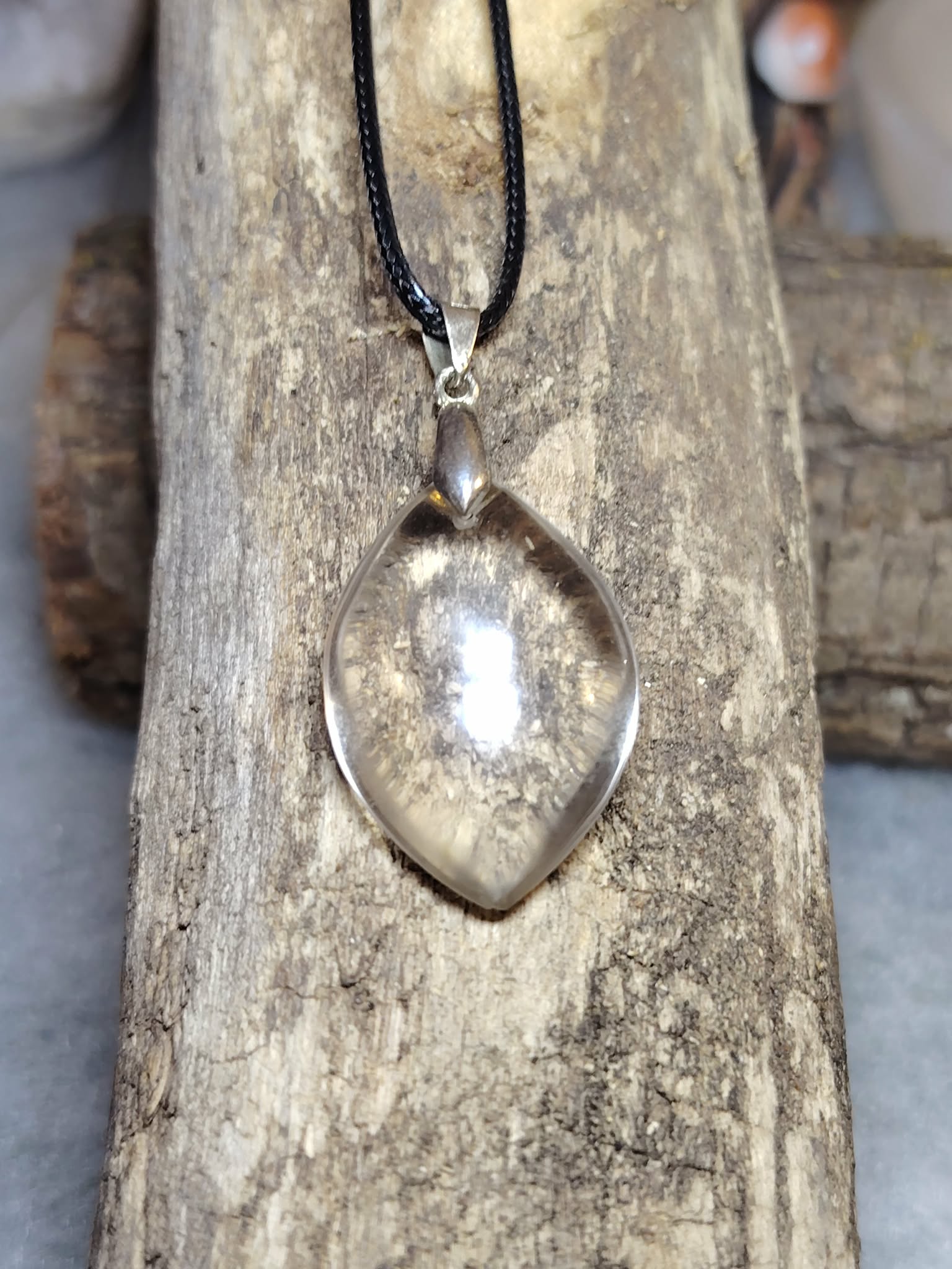 pendentif cristal de roche forme goutte suspendu sur planche bois, reflets discrets, ambiance minimaliste — harmonisation énergétique
