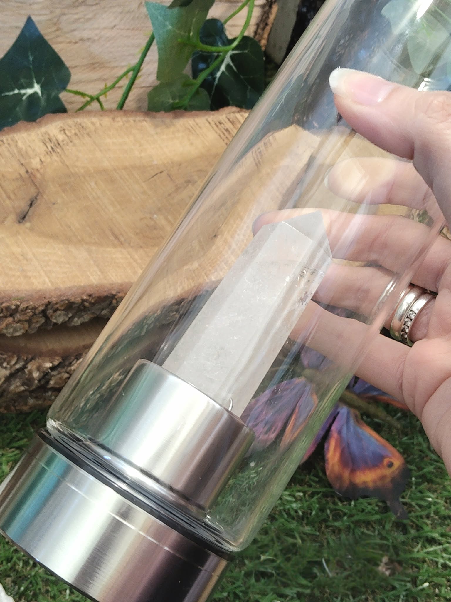 bouteille deau en verre énergisant cristal de roche, tenue en main, base inox, pointe de cristal de roche intégrée, photo sur décor nature bois