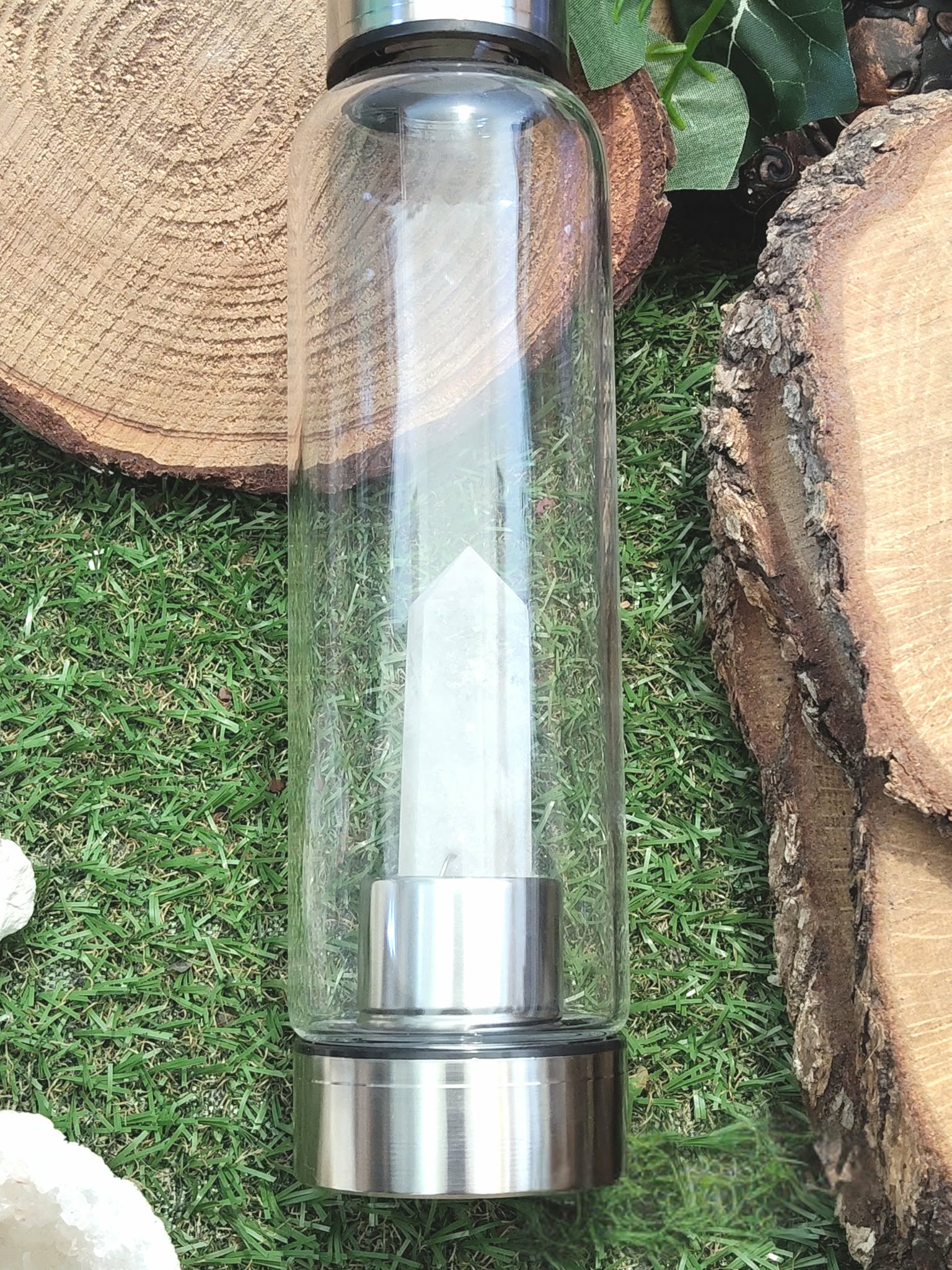 bouteille deau en verre énergisant cristal de roche, gros plan sur la pointe de cristal de roche intégrée, base inox, décor mousse verte et rondins de bois