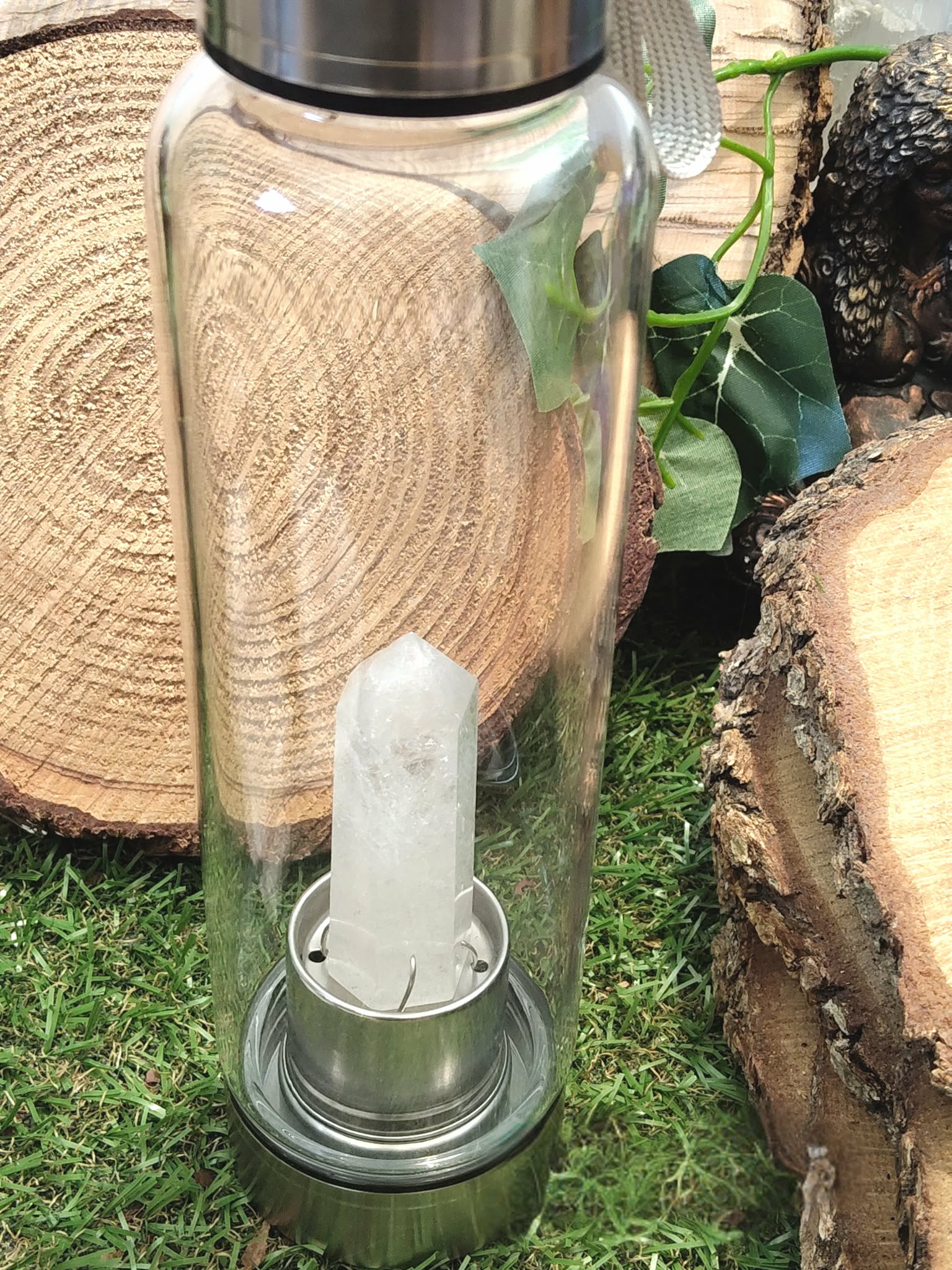 bouteille deau en verre énergisant cristal de roche, vue de côté, bouchon inox, pointe de cristal de roche intégrée, décor tranches de bois et feuillage