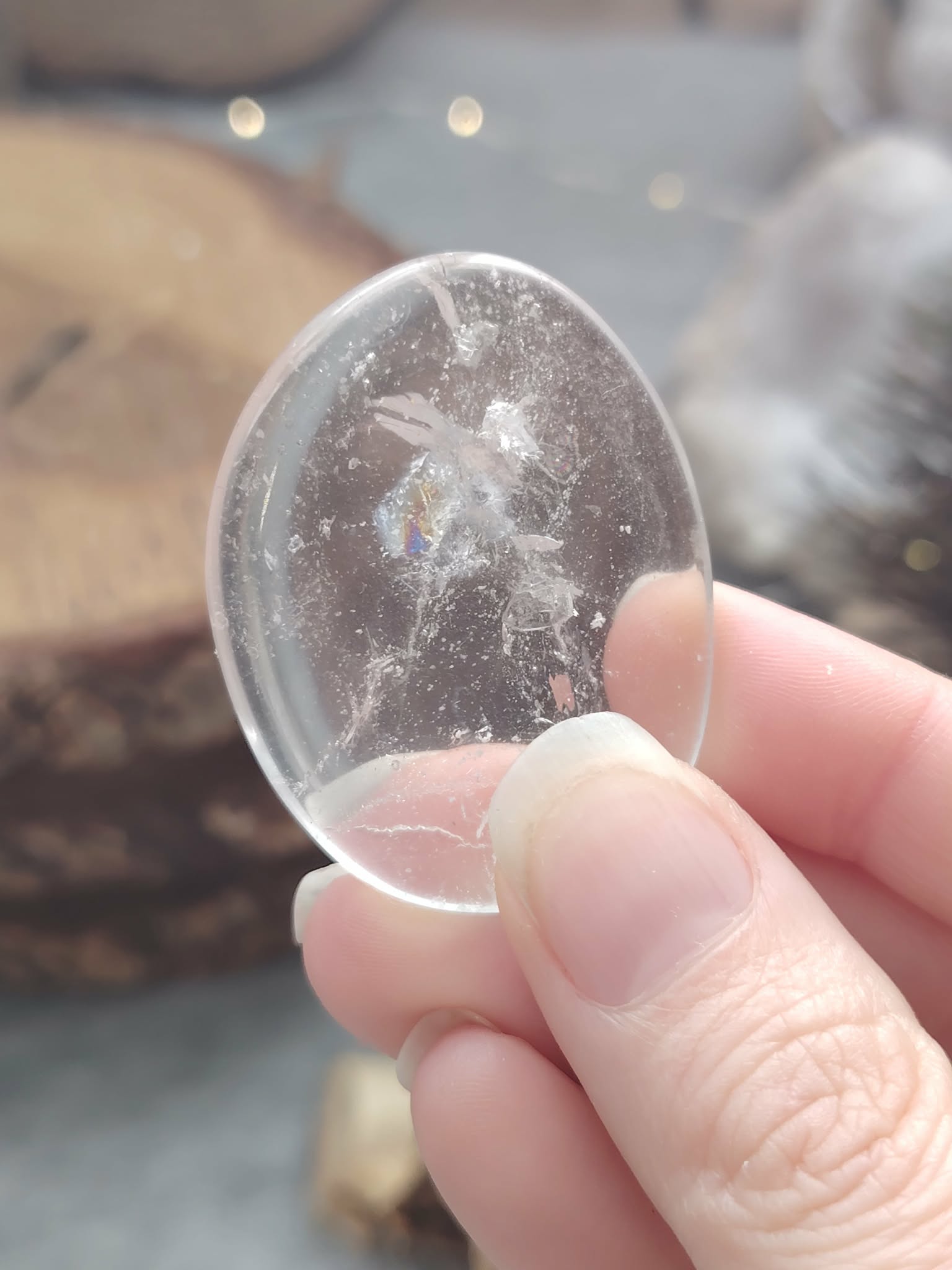 Galet cristal de roche poli tenu en main en gros plan, pierre roulée translucide avec inclusions naturelles associée à la simplicité, à la clarté et à l’équilibre intérieur.