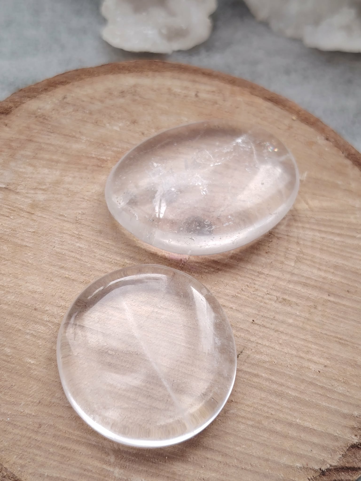 Deux galets cristal de roche polis posés sur tranche de bois en lumière naturelle, pierres translucides évoquant l’équilibre, la douceur et la clarté d’esprit.
