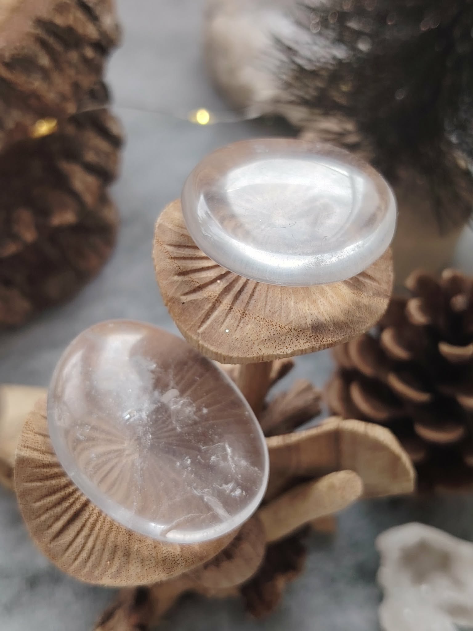 Galets cristal de roche polis posés sur rondins de bois en décor nature, pierres roulées translucides associées à l’harmonisation, à la lumière intérieure et à la sérénité.