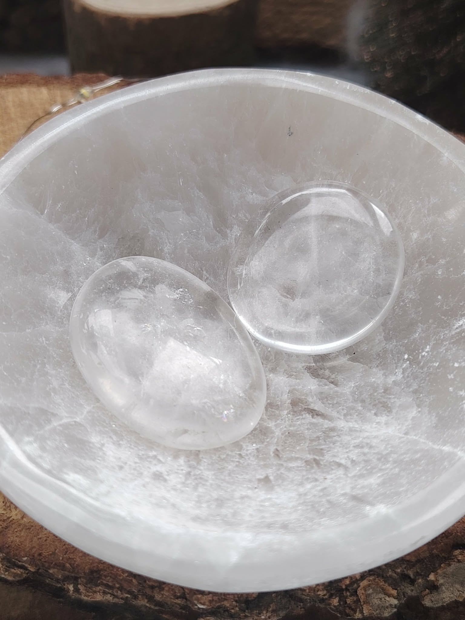 Galets cristal de roche polis en gros plan, posés dans un bol en sélénite, pierres translucides liées à la purification, au calme du mental et à l’harmonie intérieure.