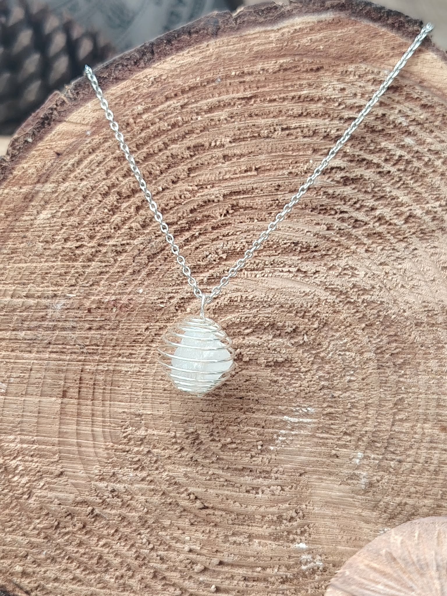 Pendentif cage spirale avec pierre blanche (cristal de roche), sur tranche de bois — associé à la clarté mentale et à l’harmonisation