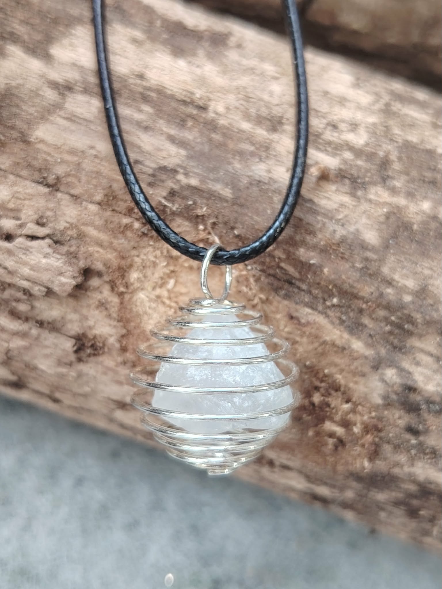Pendentif cage spirale avec amas de quartz (cristal de roche), cordon noir, posé sur bois brut, pierre d’amplification et clarté.