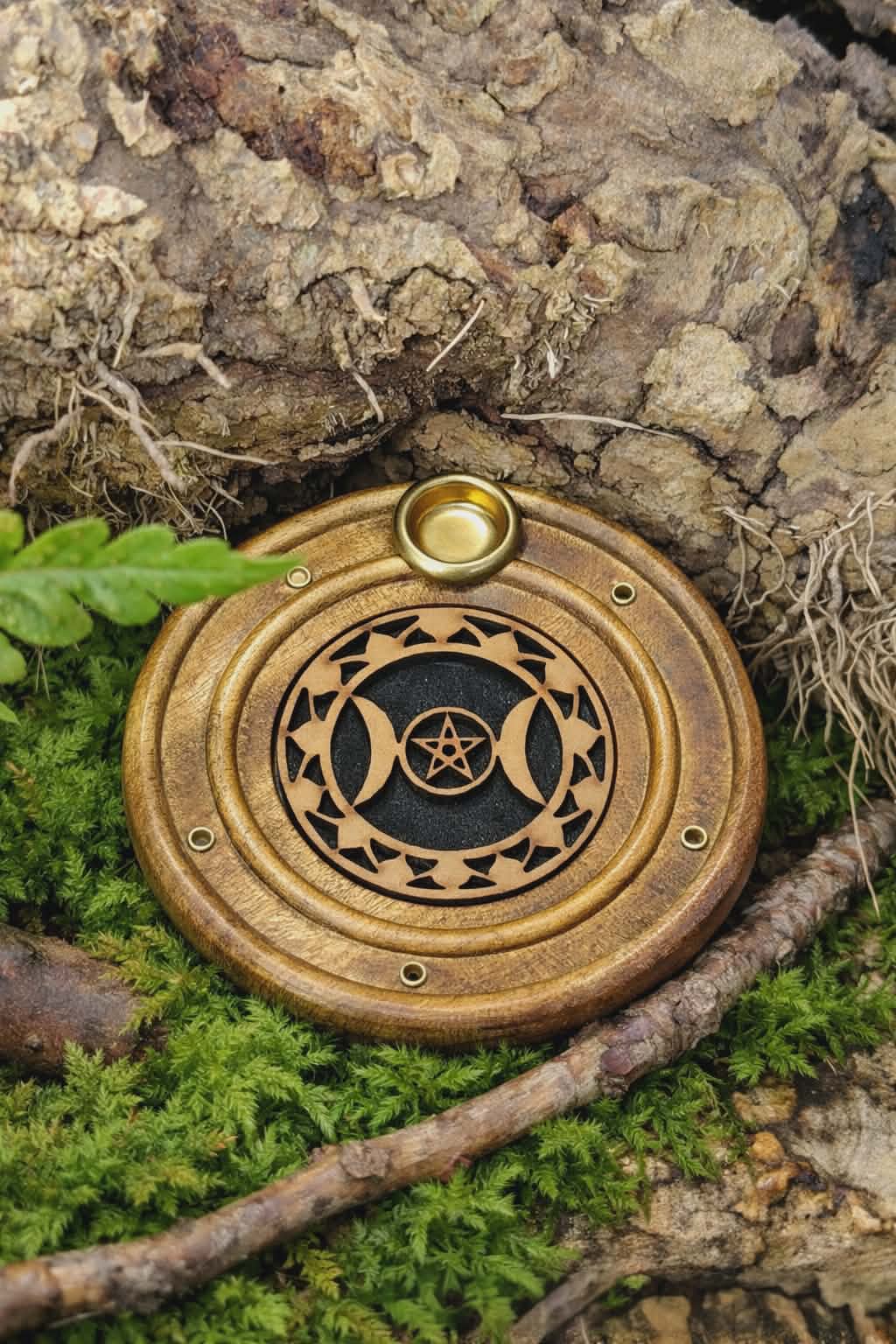 Porte-encens rond en bois motif Triple Lune, posé sur de la mousse verte au pied d’une écorce, ambiance forêt.