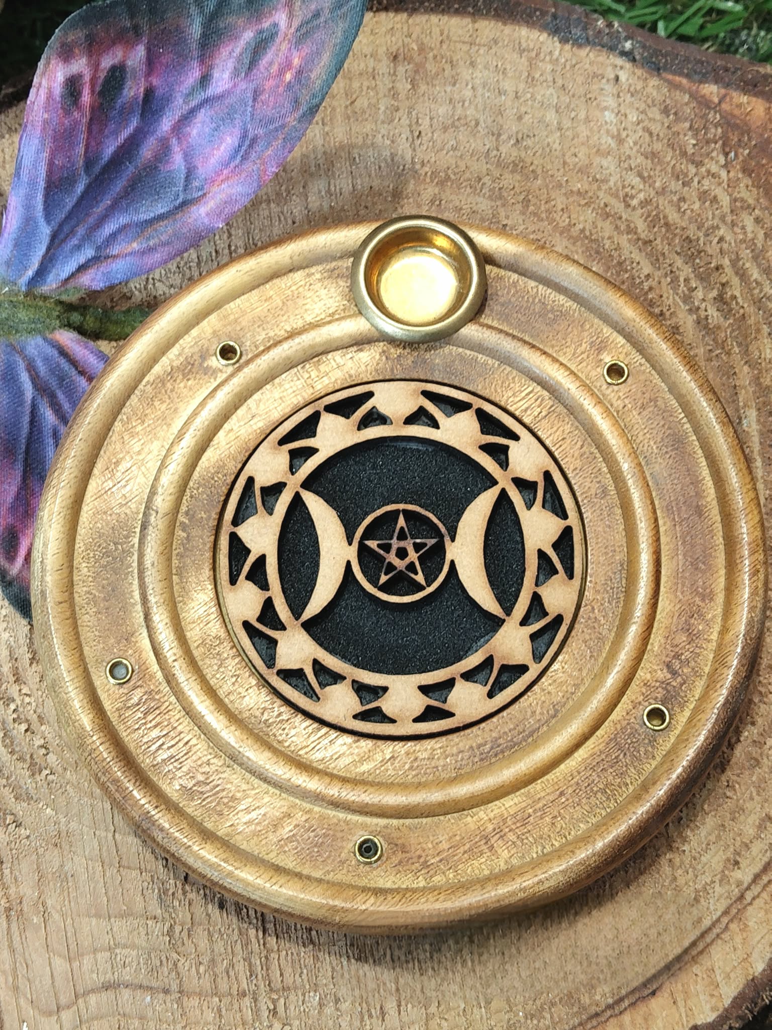 Porte-encens rond en bois motif Triple Lune, posé sur une tranche de bois avec une aile/papillon violet en décor sur le côté.
