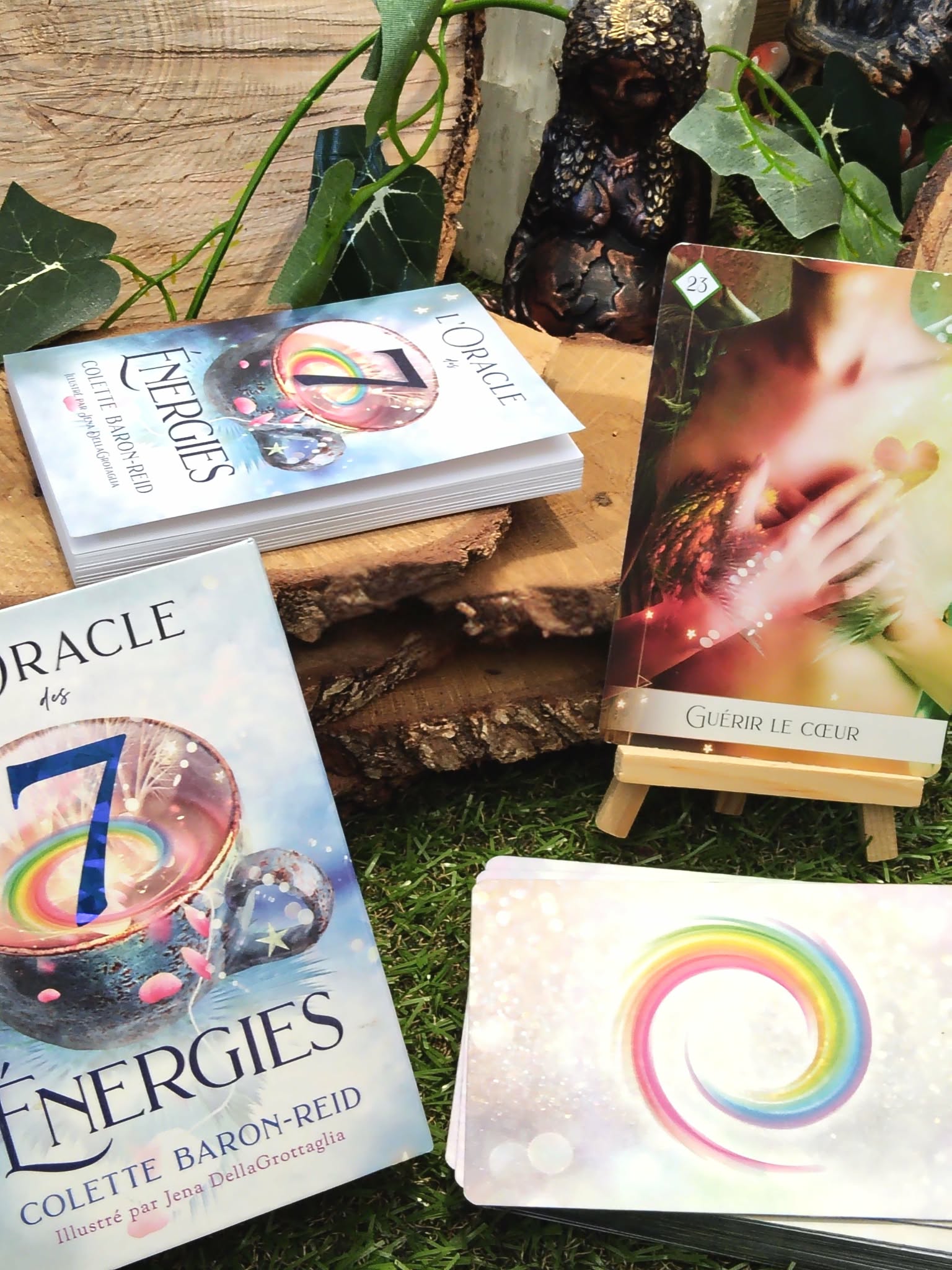 L’Oracle des 7 Énergies – coffret divinatoire en français avec boîte, cartes et dos au cercle multicolore, mise en scène sur mousse/bois avec feuillage et petit chevalet en bois.