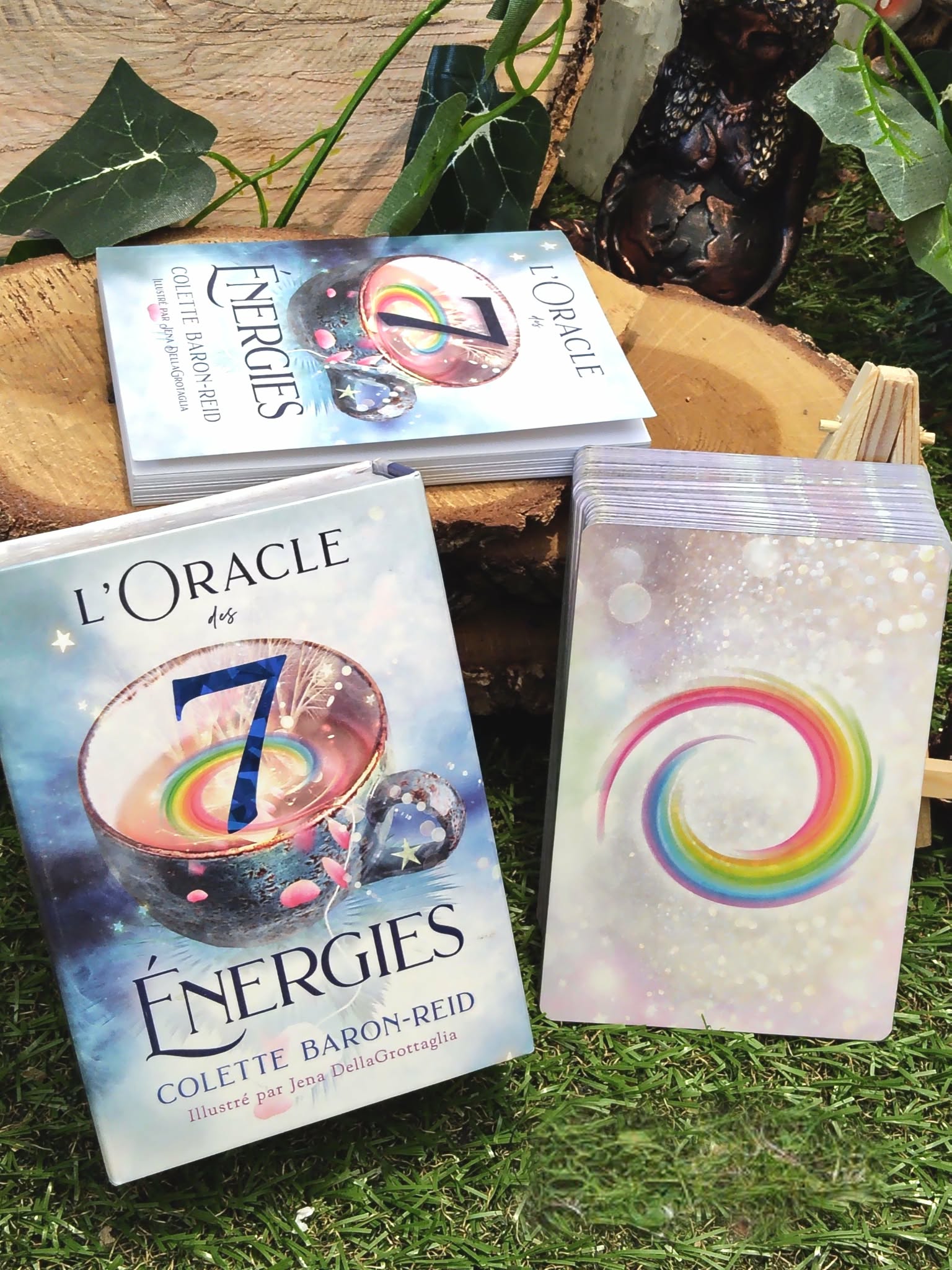 L’Oracle des 7 Énergies – coffret divinatoire en français avec boîte et une carte au motif cercle multicolore, mise en scène sur tapis vert/mousse avec éléments naturels en arrière-plan.