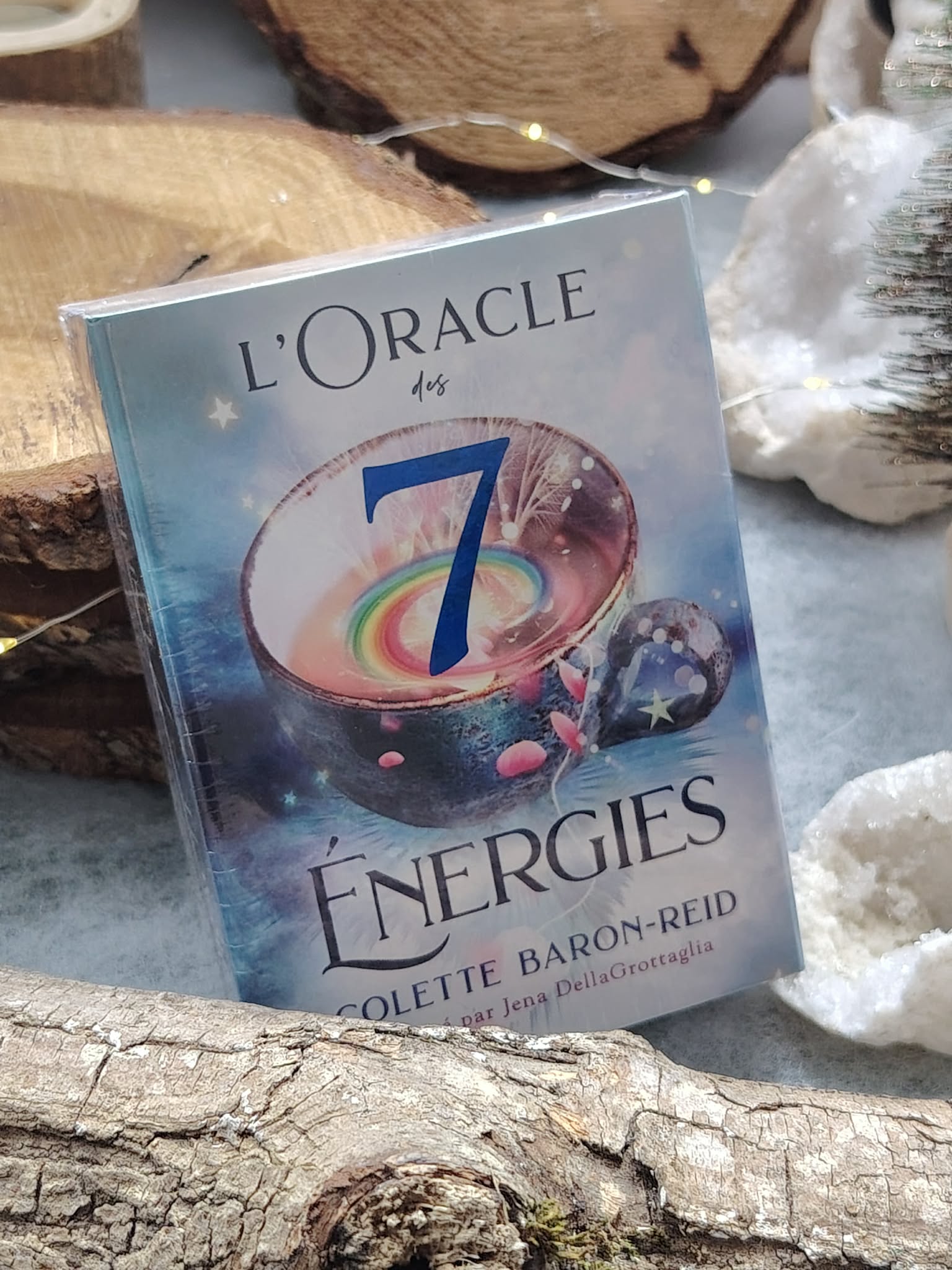 Coffret « L’Oracle des 7 Énergies » (Colette Baron-Reid) posé sur bois naturel, ambiance ésotérique avec pierres claires autour, jeu 49 cartes   livret en français.