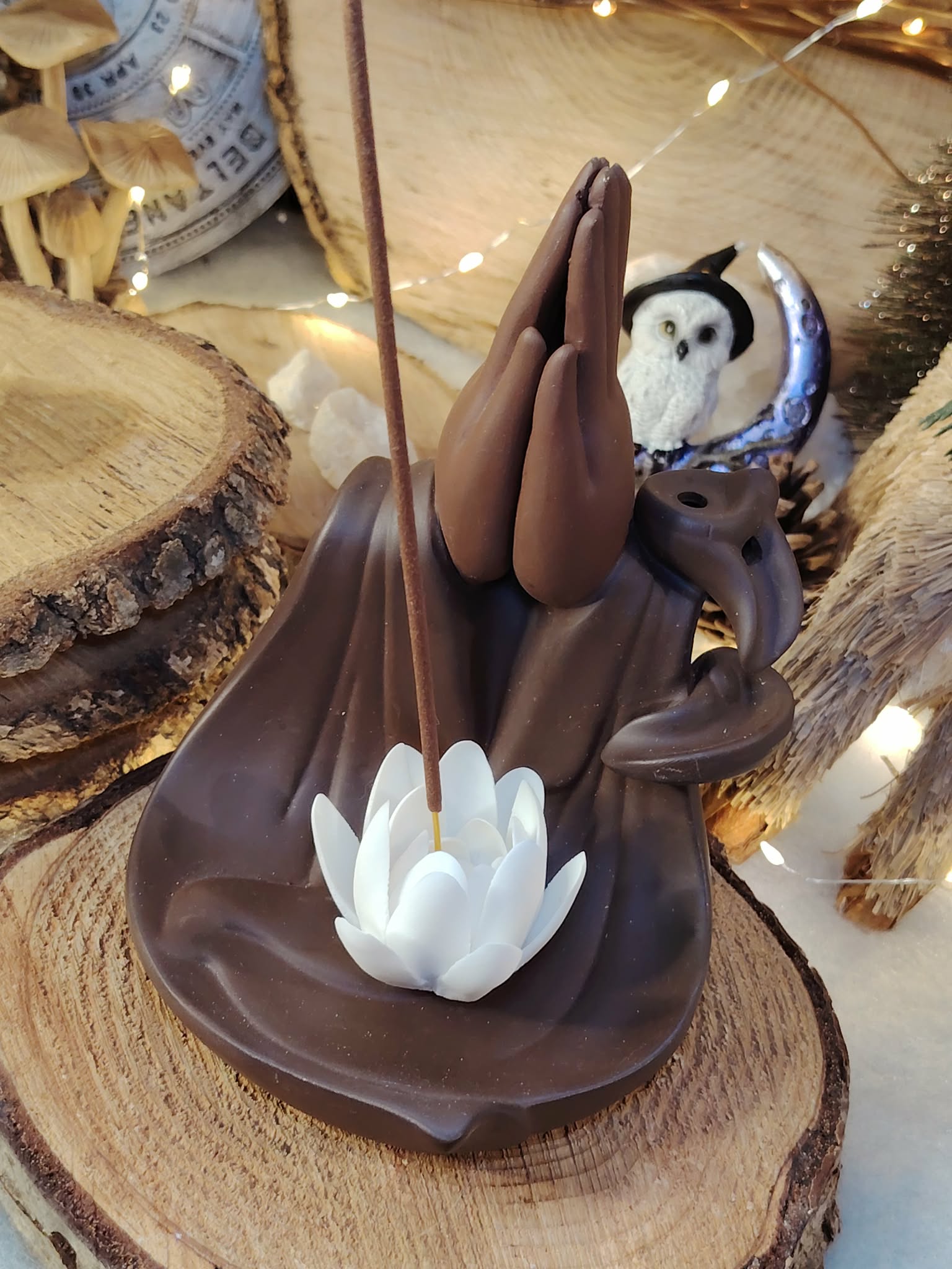 Porte-encens pour cônes backflow Mains Lotus, gros plan sur le lotus blanc, décor bois brut et accessoires spirituels derrière.
