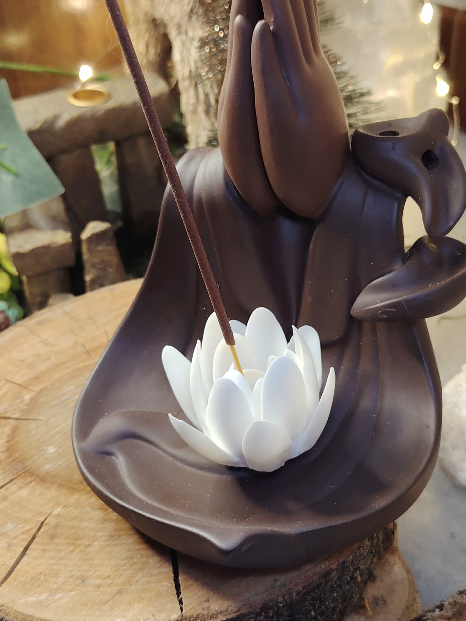 Porte-encens pour cônes backflow Mains Lotus, gros plan sur le lotus blanc, décor bois brut et accessoires spirituels derrière.