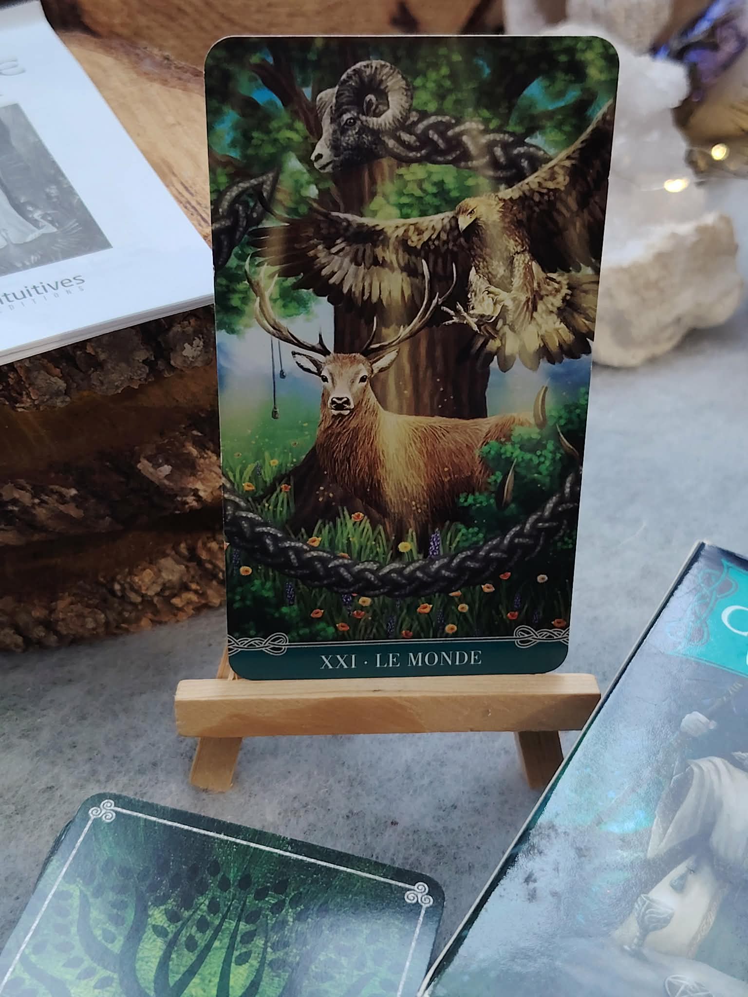 Carte du Tarot Celtique Universel sur chevalet en bois, boîtes du jeu ouvertes sur table, ambiance ésotérique