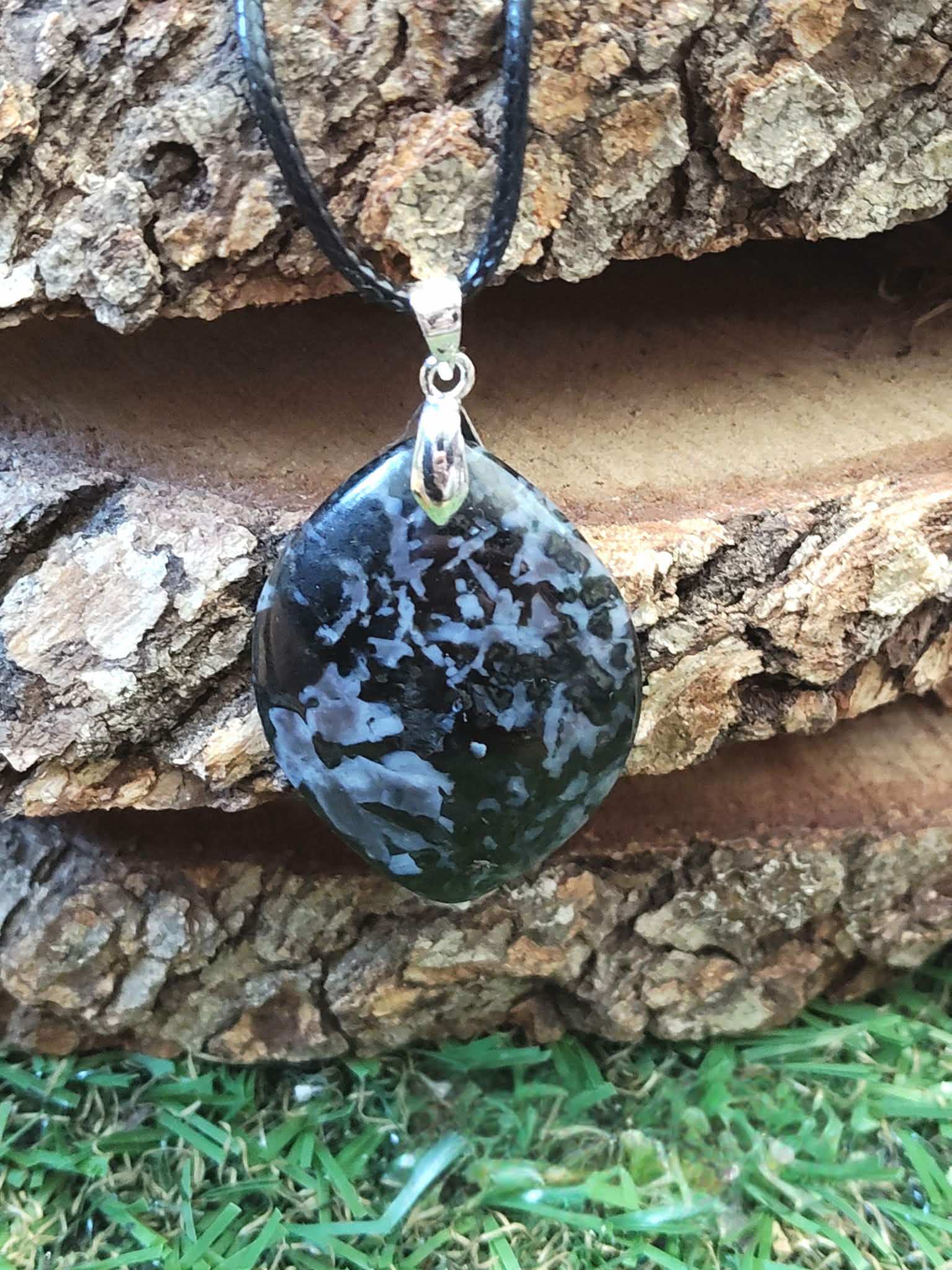Pendentif indigo gabbro poli suspendu devant rondins en ambiance nature, pierre naturelle associée à la stabilité émotionnelle, à l’aplomb et au recentrage.