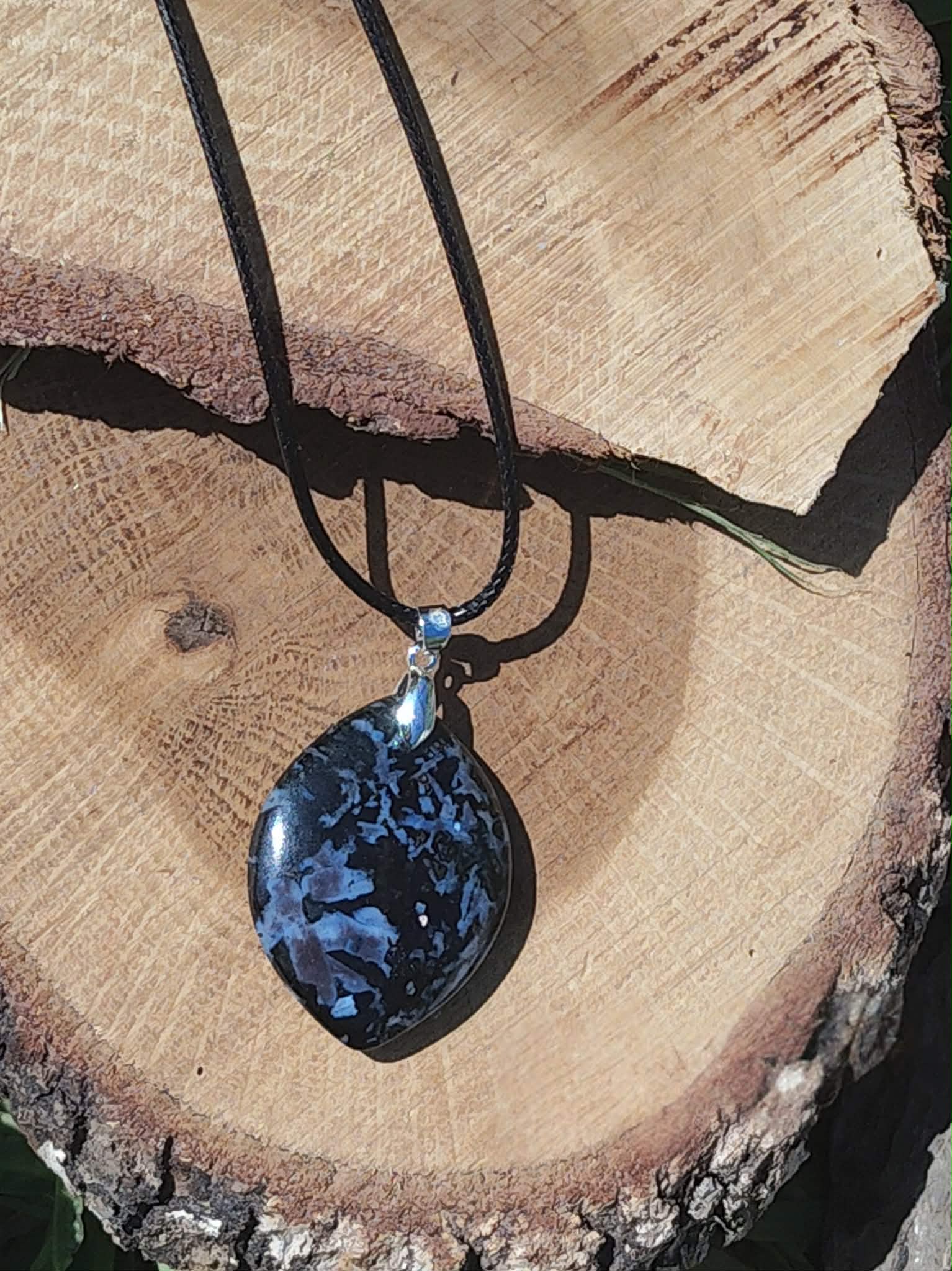 Pendentif indigo gabbro en forme de goutte sur cordon noir, présenté sur bois brut, bijou en pierre naturelle évoquant la force calme, la stabilité et les nouveaux élans.
