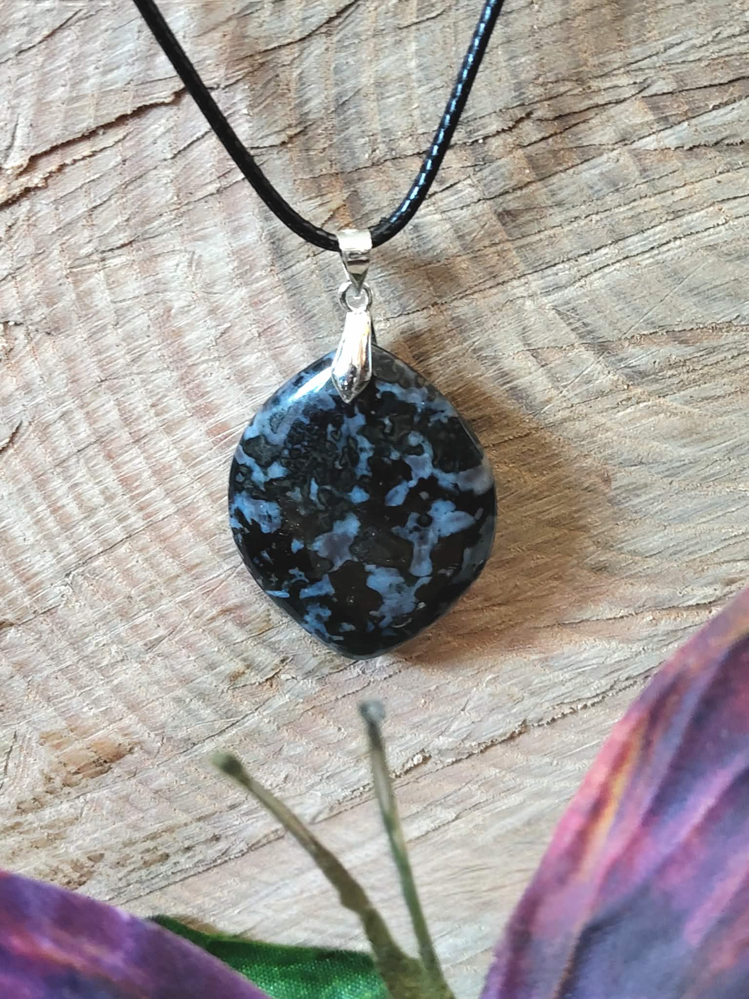 Pendentif indigo gabbro en gros plan sur rondin de bois, pierre naturelle sombre associée à la clarté d’esprit, à l’équilibre émotionnel et à la stabilité profonde.