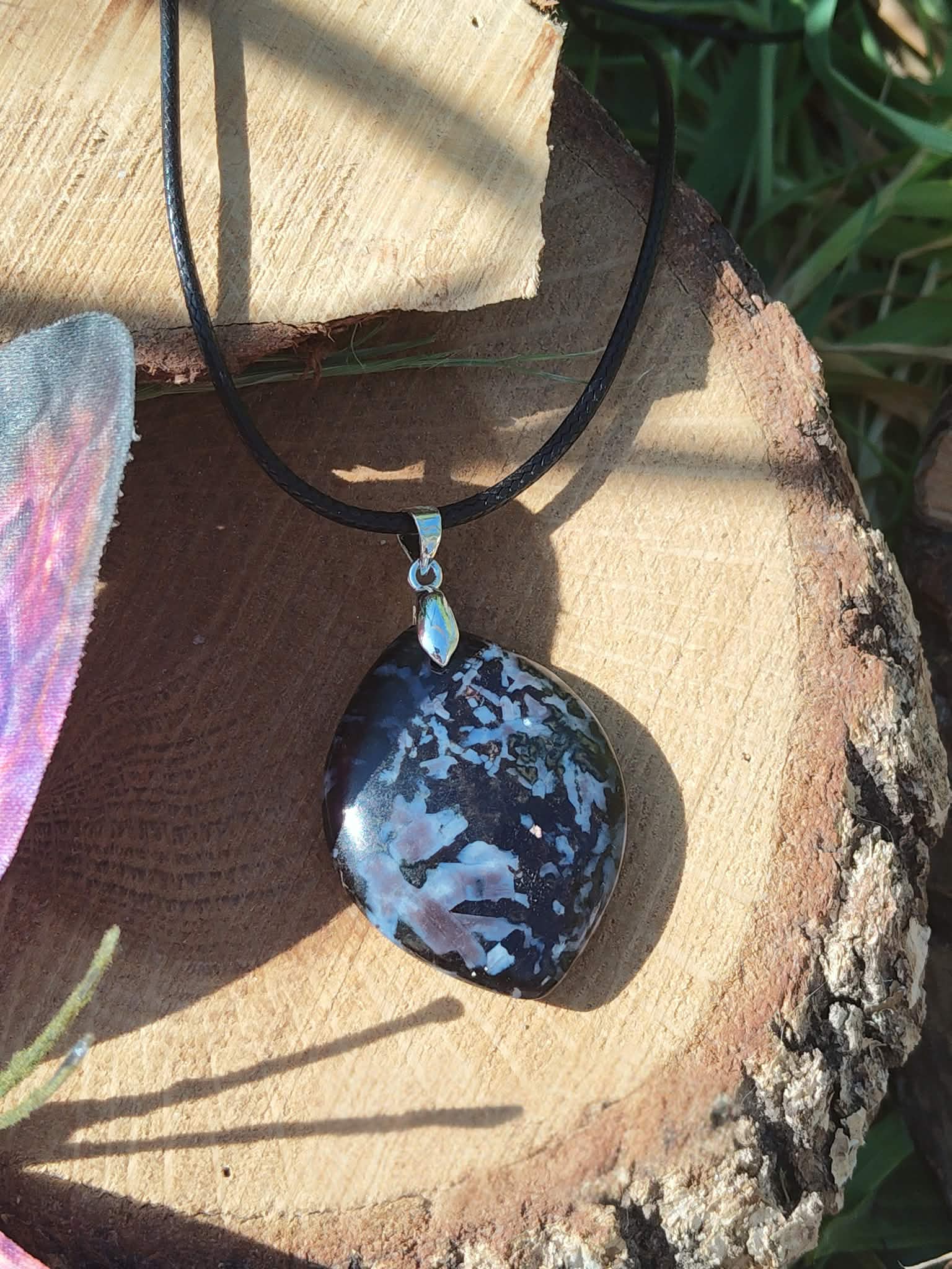 Pendentif goutte en gabbro sur cordon noir, posé sur rondin de bois avec décor ésotérique, pierre naturelle associée au recentrage, à la stabilité intérieure et à l’ancrage.