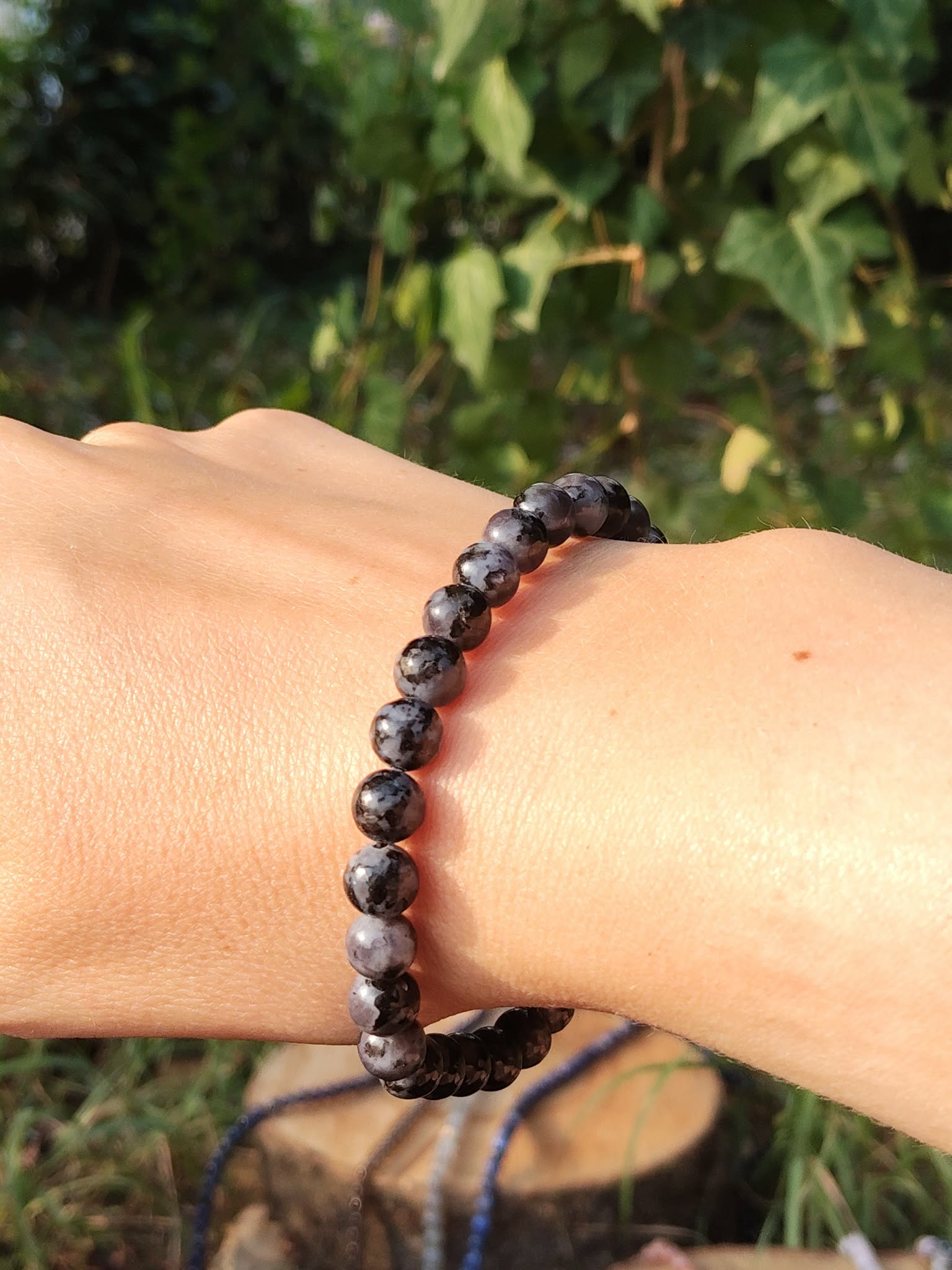 Bracelet Gabbro porté au poignet, perles bleu-noir en extérieur sur fond feuillage, bijou en pierre naturelle pour ancrage et stabilité