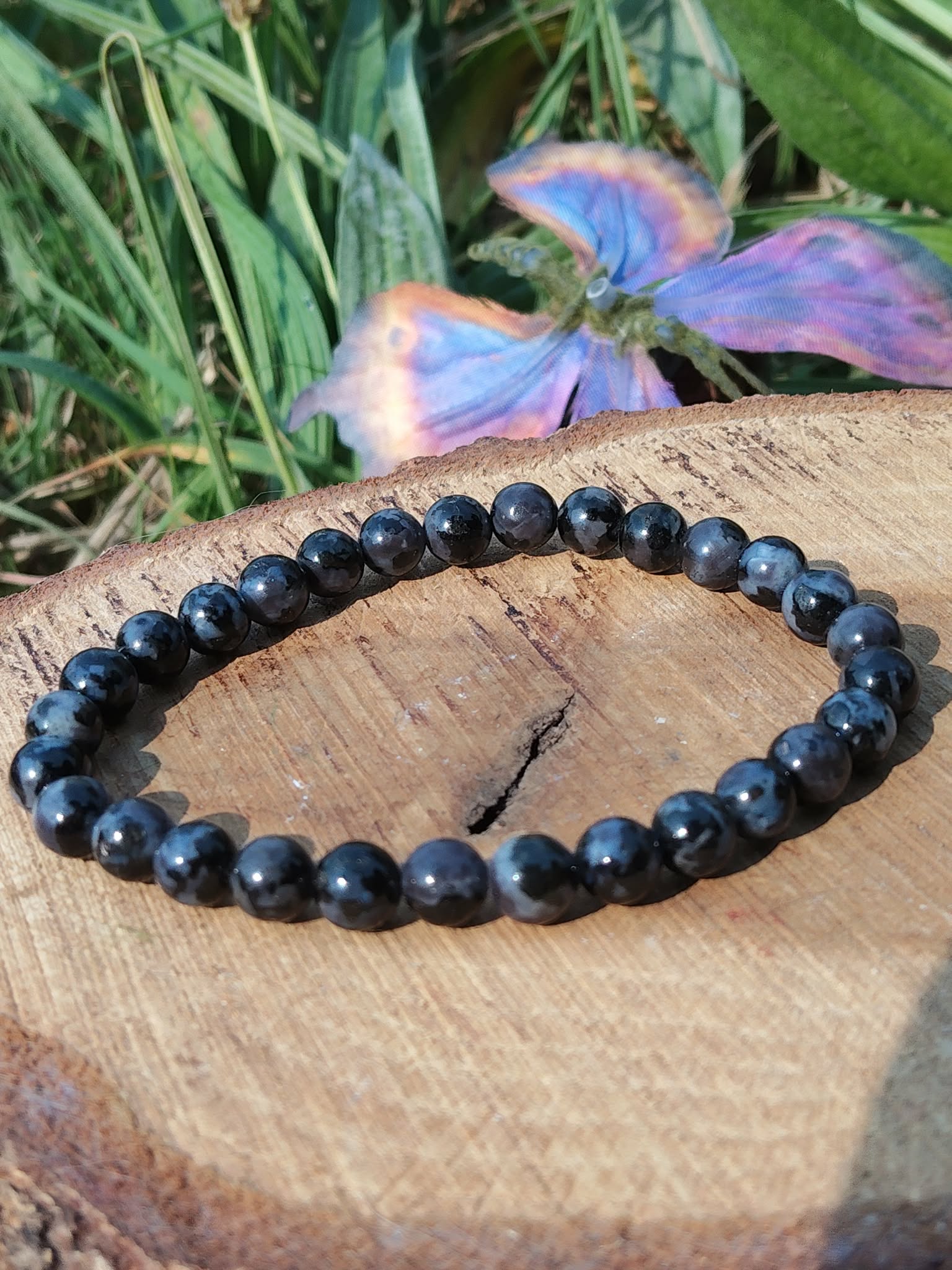 Bracelet Indigo Gabbro perles polies sur rondin, feuillage vert en arrière-plan, pierre naturelle liée à l’équilibre émotionnel