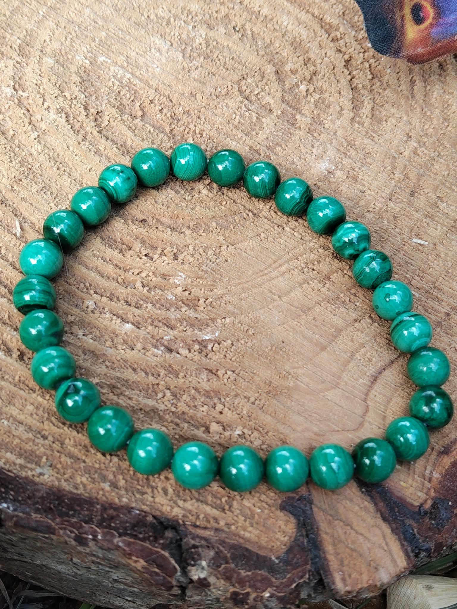 Bracelet en malachite naturelle sur tranche de bois, perles rondes vert marbré, énergie du cœur et équilibre émotionnel.