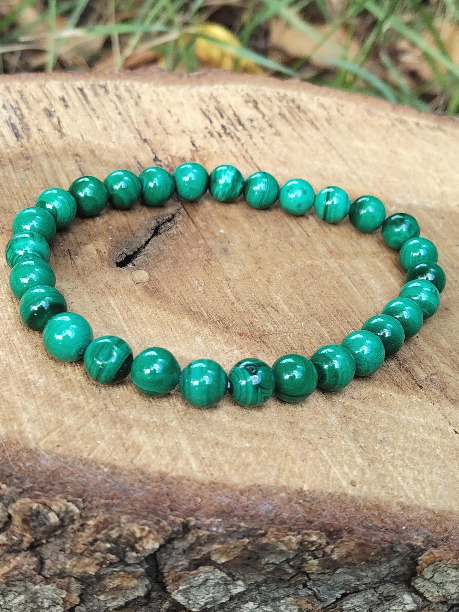 Bracelet en malachite sur rondin de bois, perles vertes veinées et fond végétal, création nature liée au calme intérieur